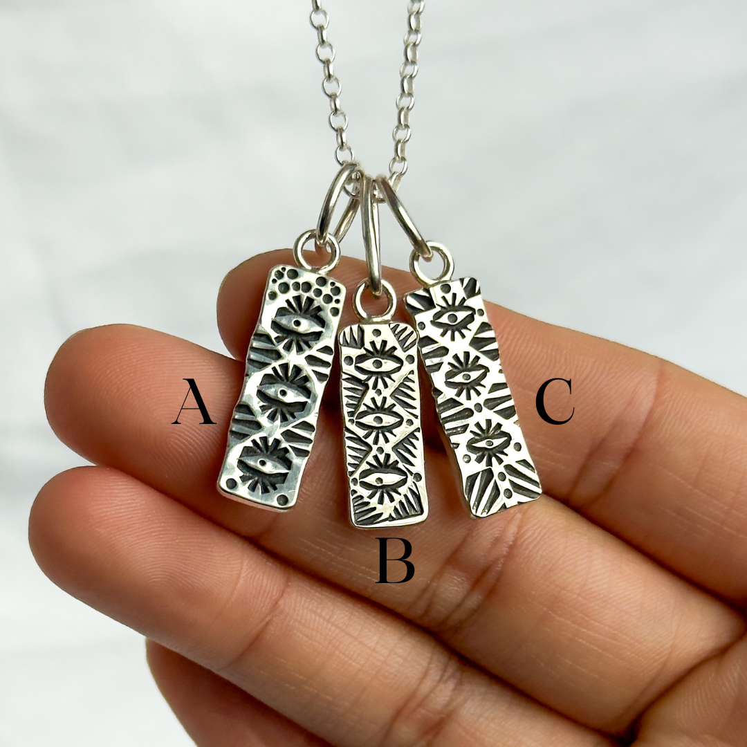 Three silver pendant tags on a chain held in a hand with a white background