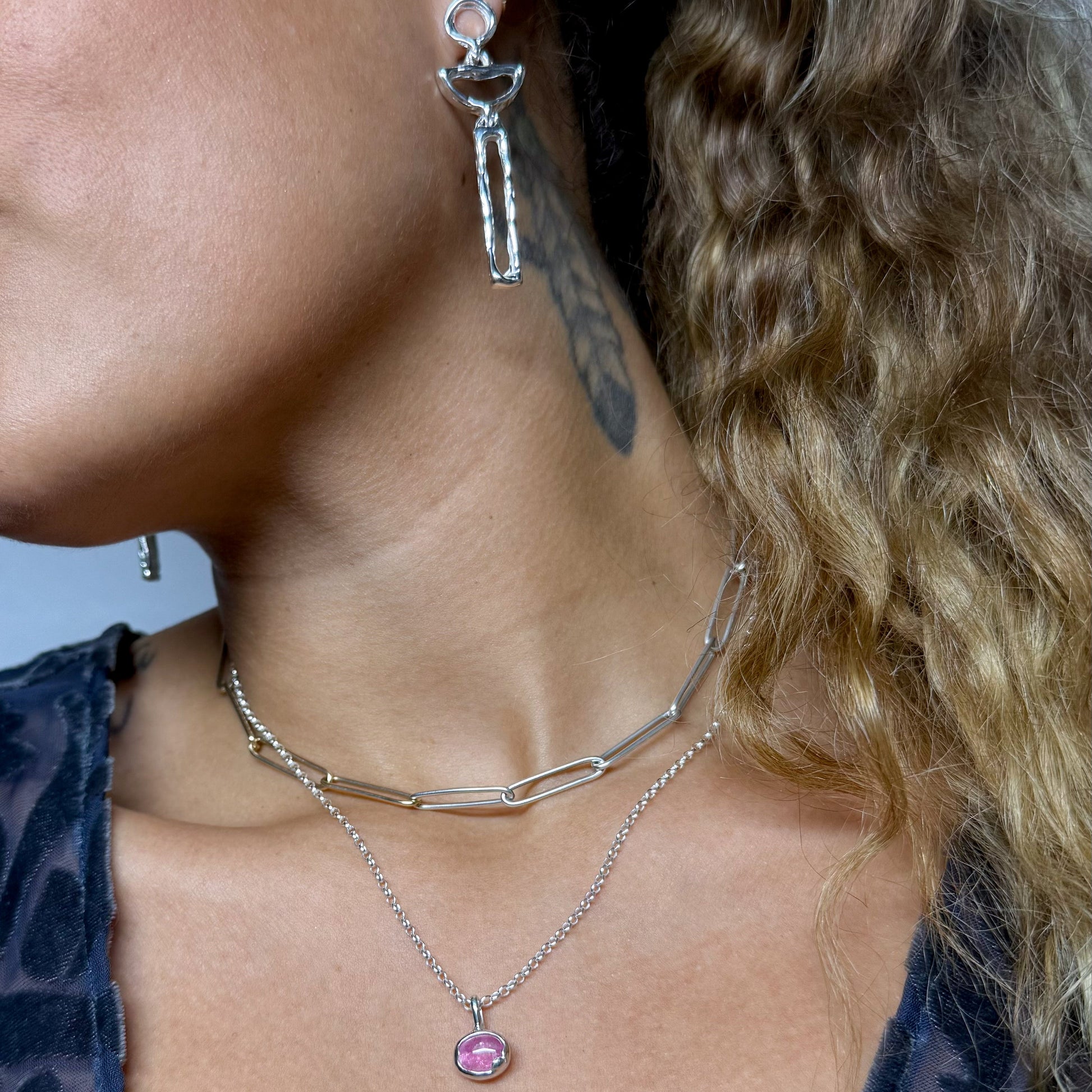Close-up of a person wearing a silver necklace with a pink tourmaline pendant and silver earrings.
