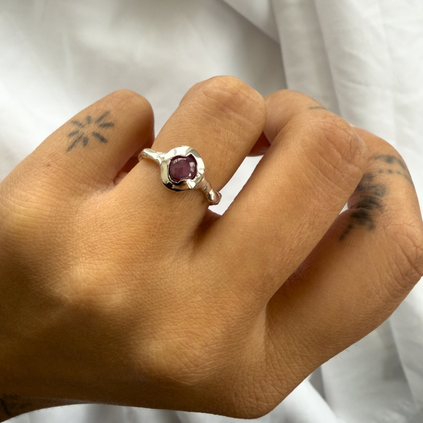 Hand wearing a ring with a purple gemstone against a white background