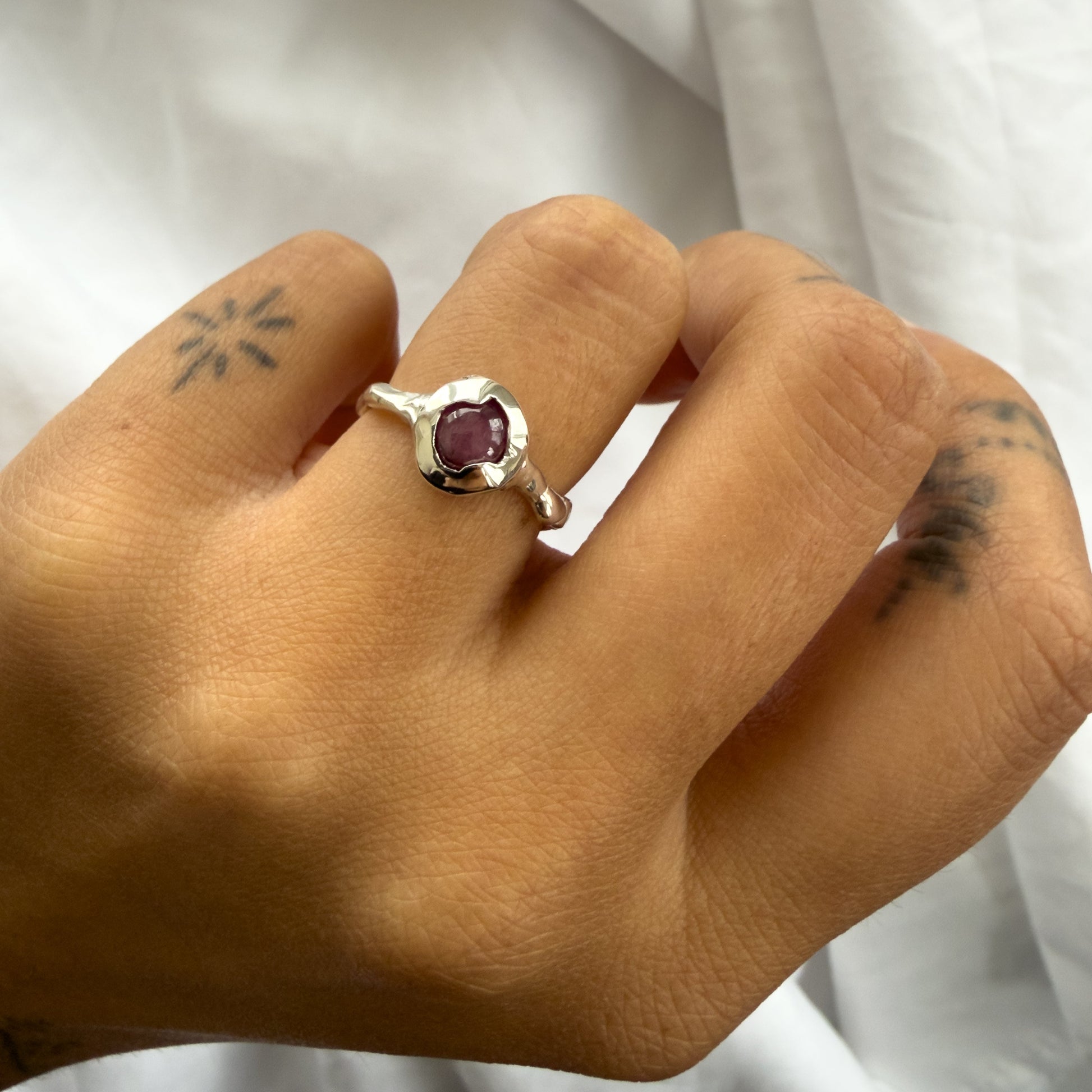 Hand wearing a ring with a purple gemstone against a white background