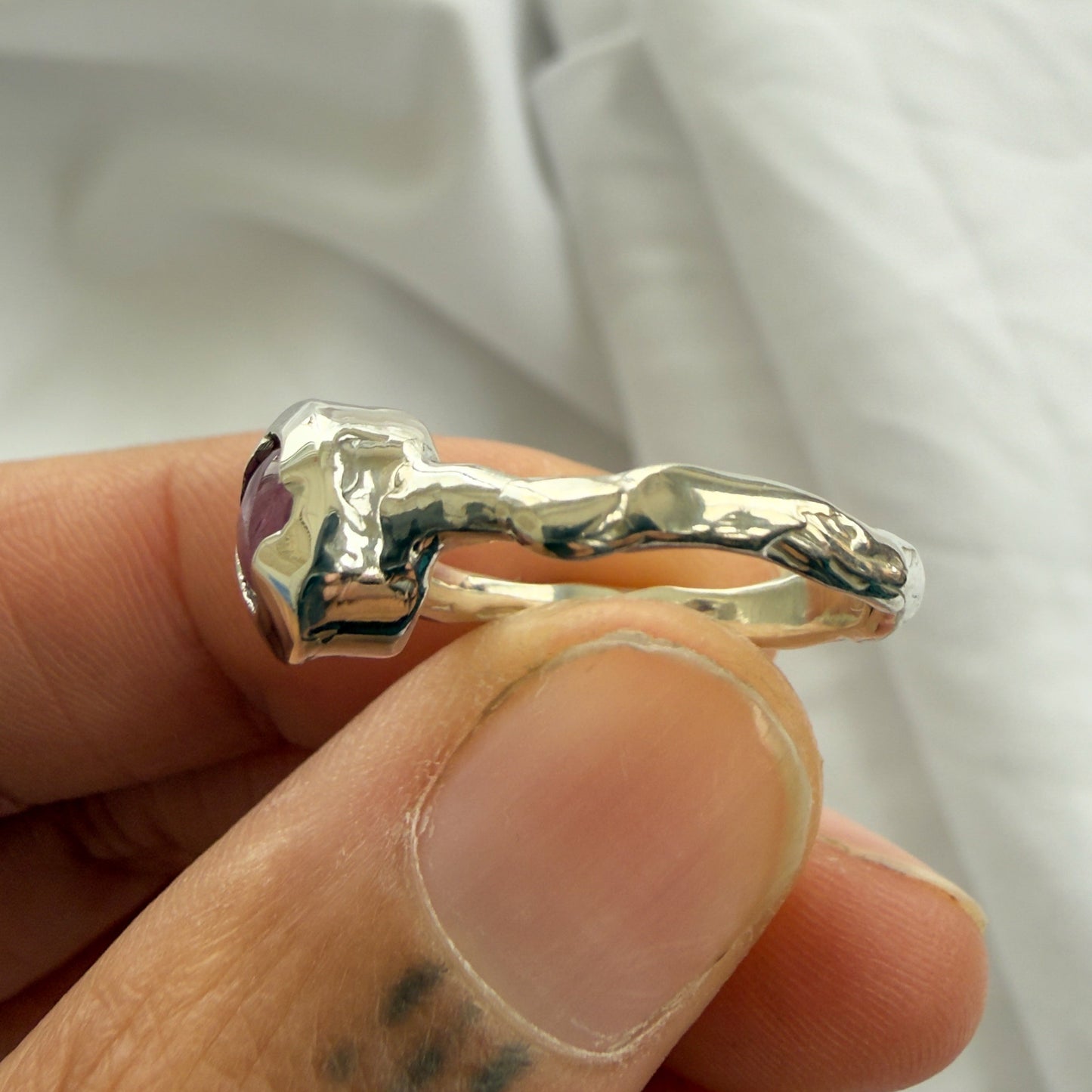 Silver ring with a unique design held by a finger against a white background