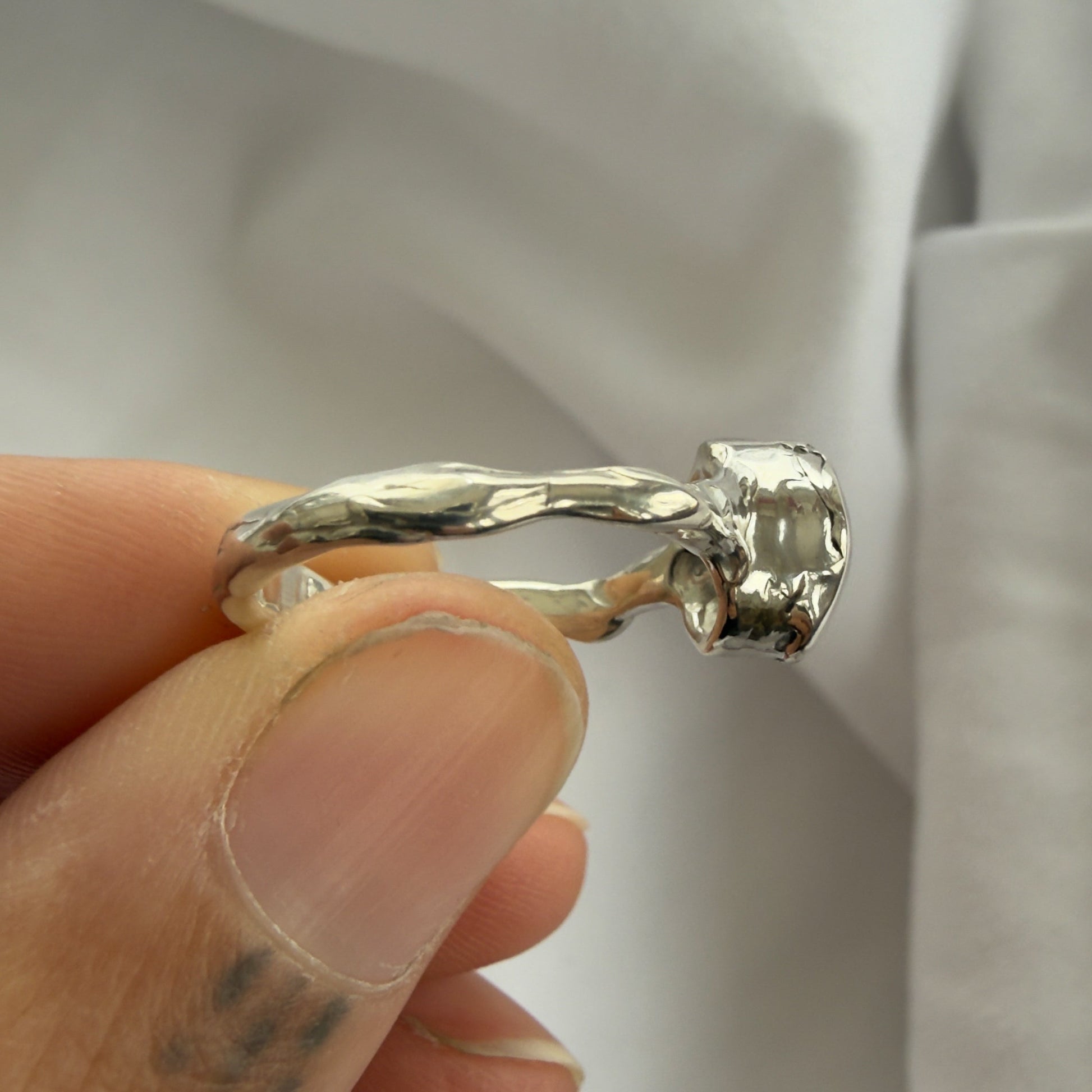 Silver ring held between fingers against a neutral background