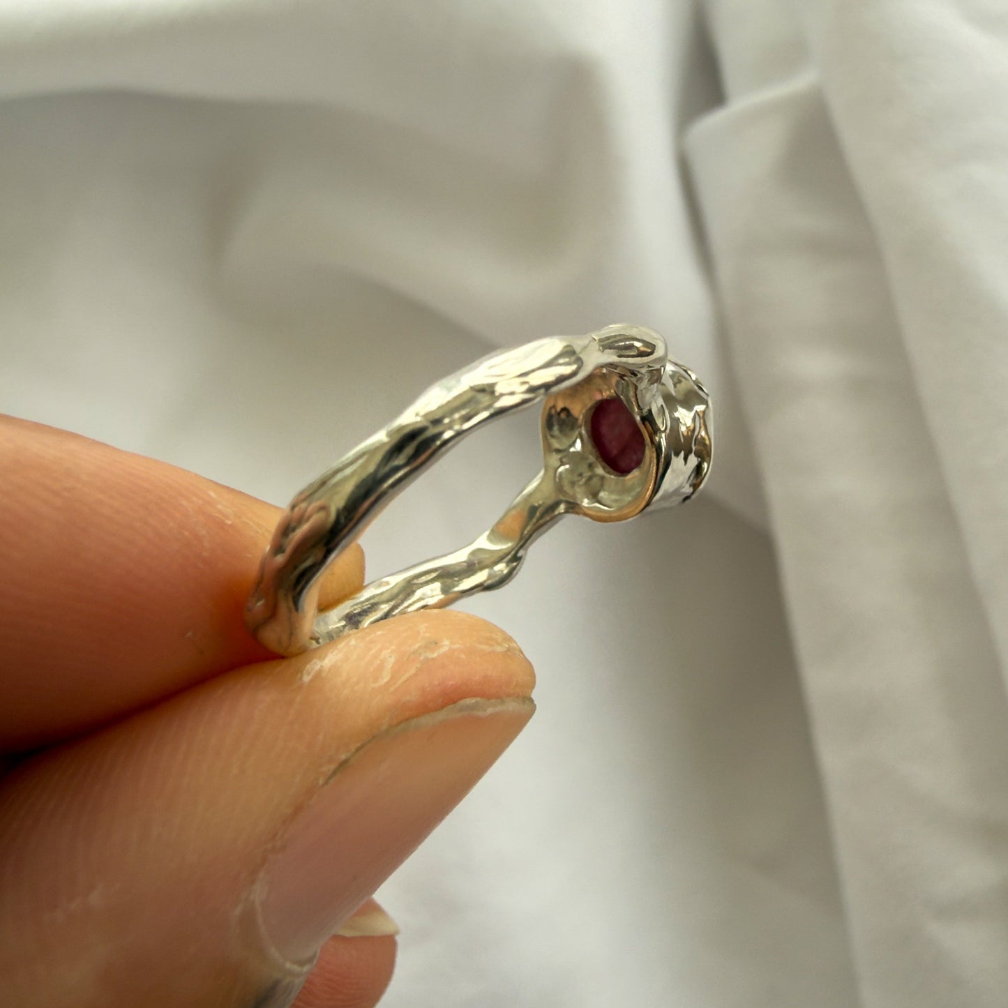 Silver ring with a red gemstone held by a hand against a white background