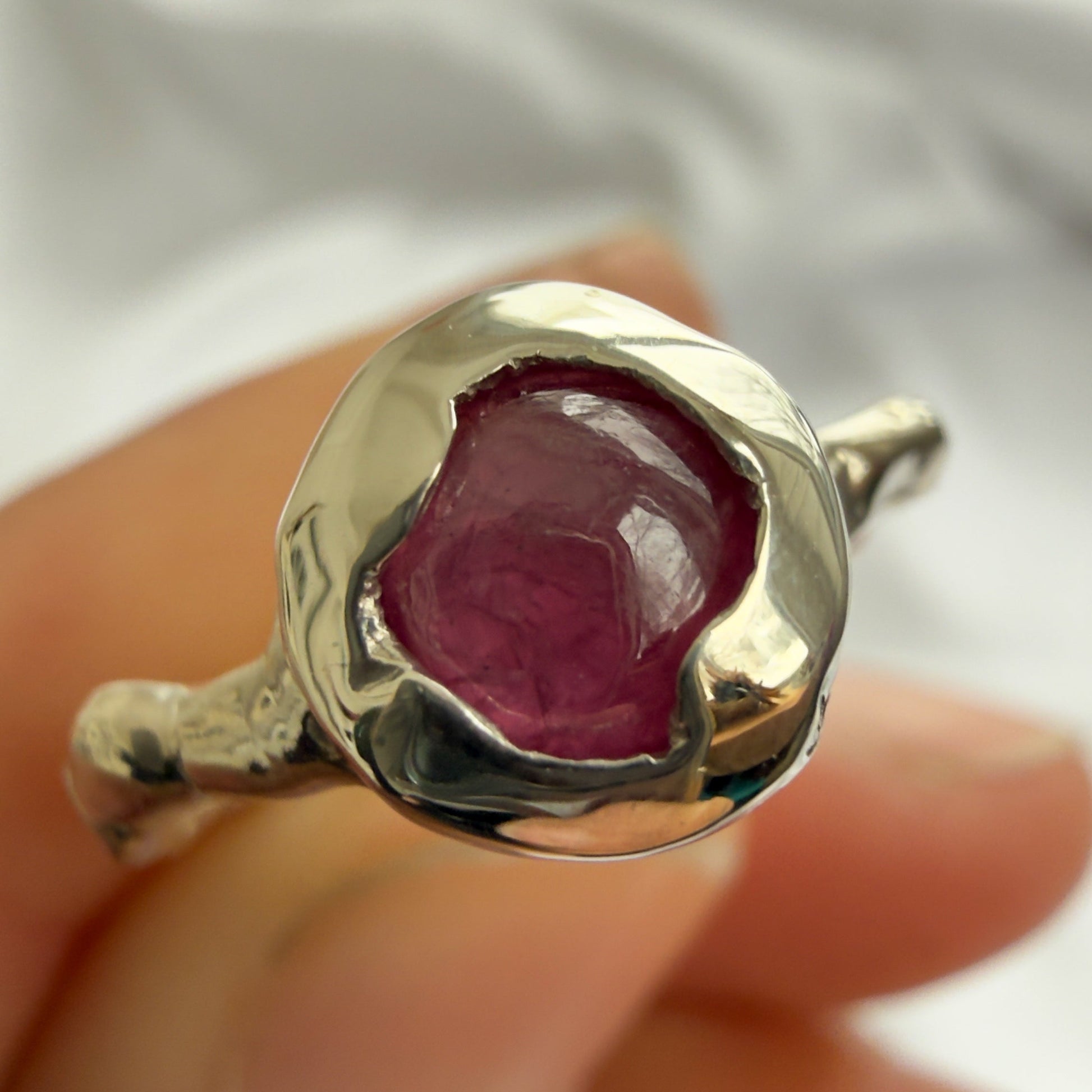 silver ring with a red gemstone held in a hand against a white background