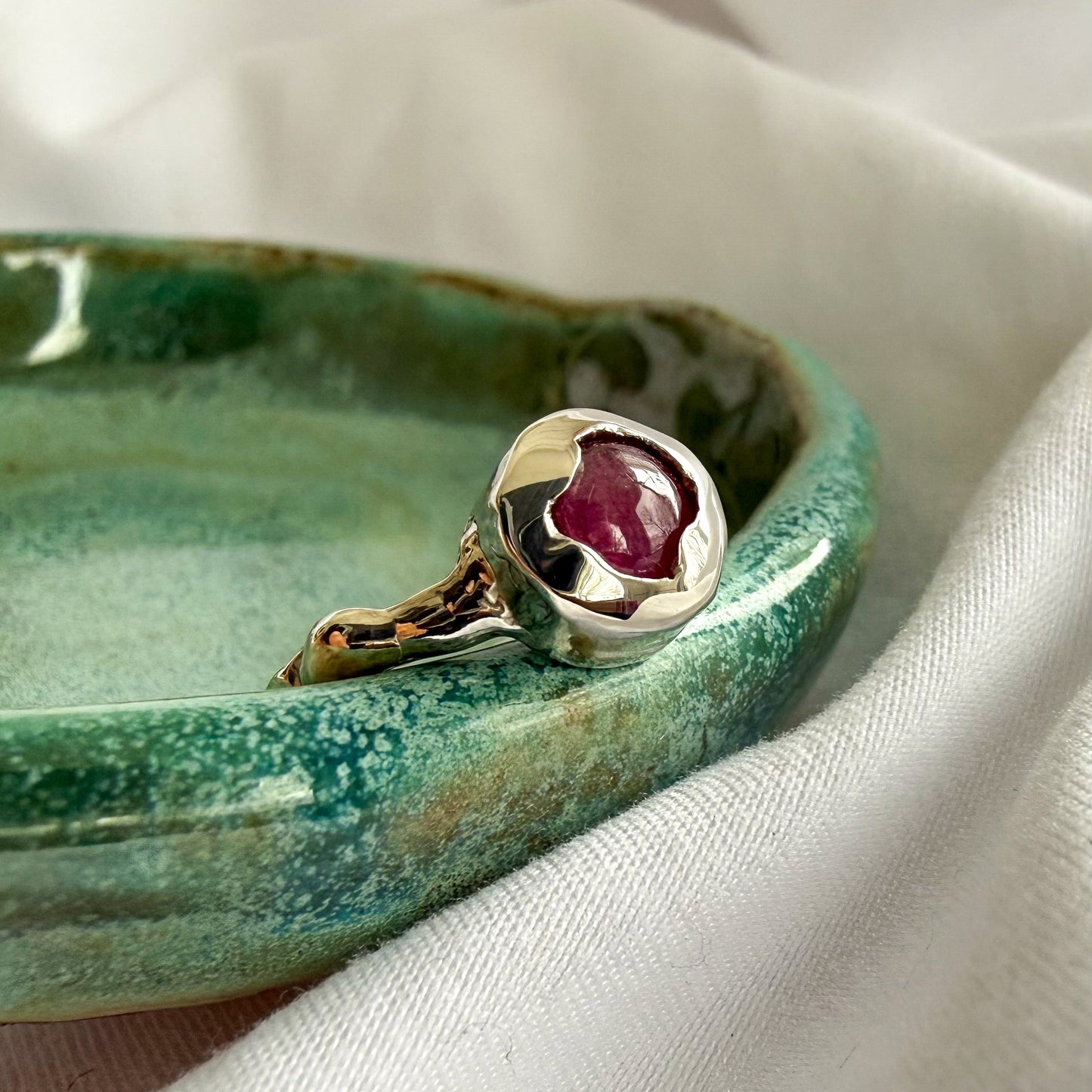 silver ring with a red gemstone on a green ceramic dish