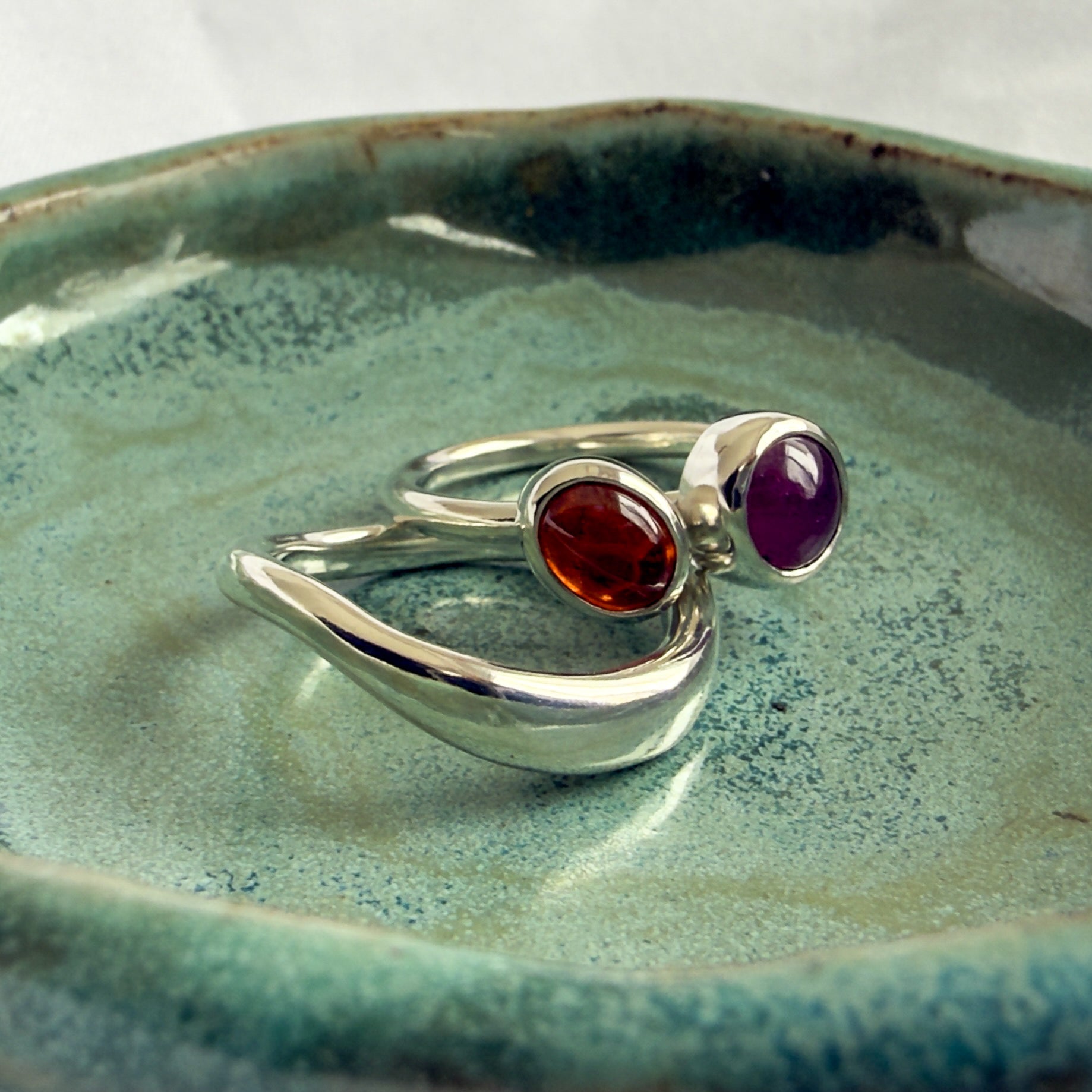 Silver ring with red and purple gemstones on a textured green surface