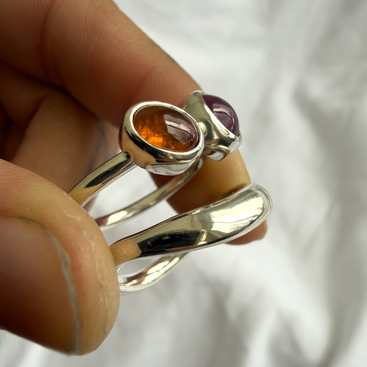 Silver ring with gemstones held by a hand against a white background