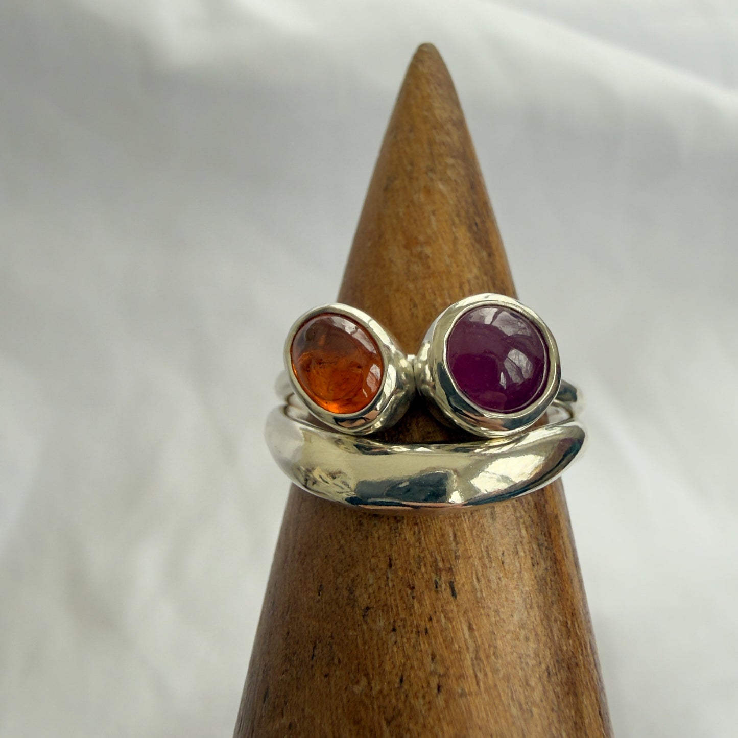 Silver ring with red and orange gemstones on a wooden stand against a white background