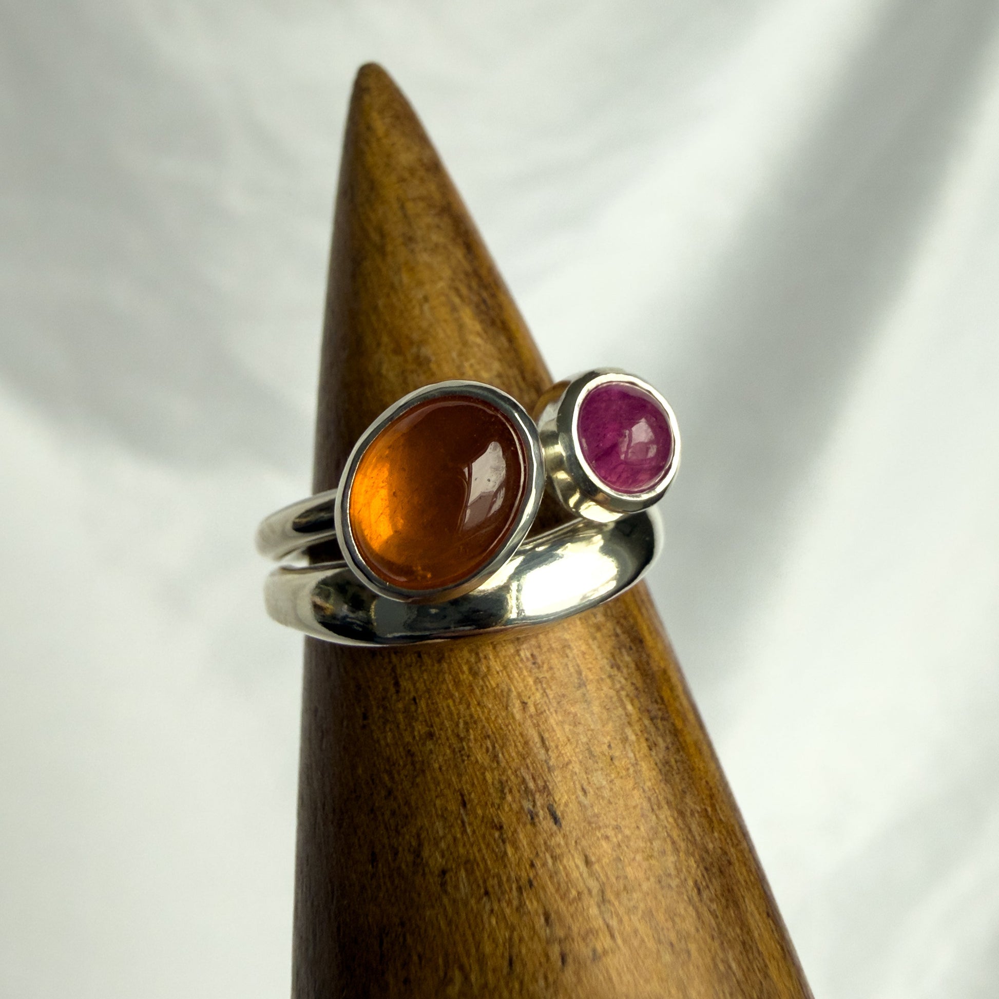 Silver ring with amber and ruby stones on a wooden stand against a white background