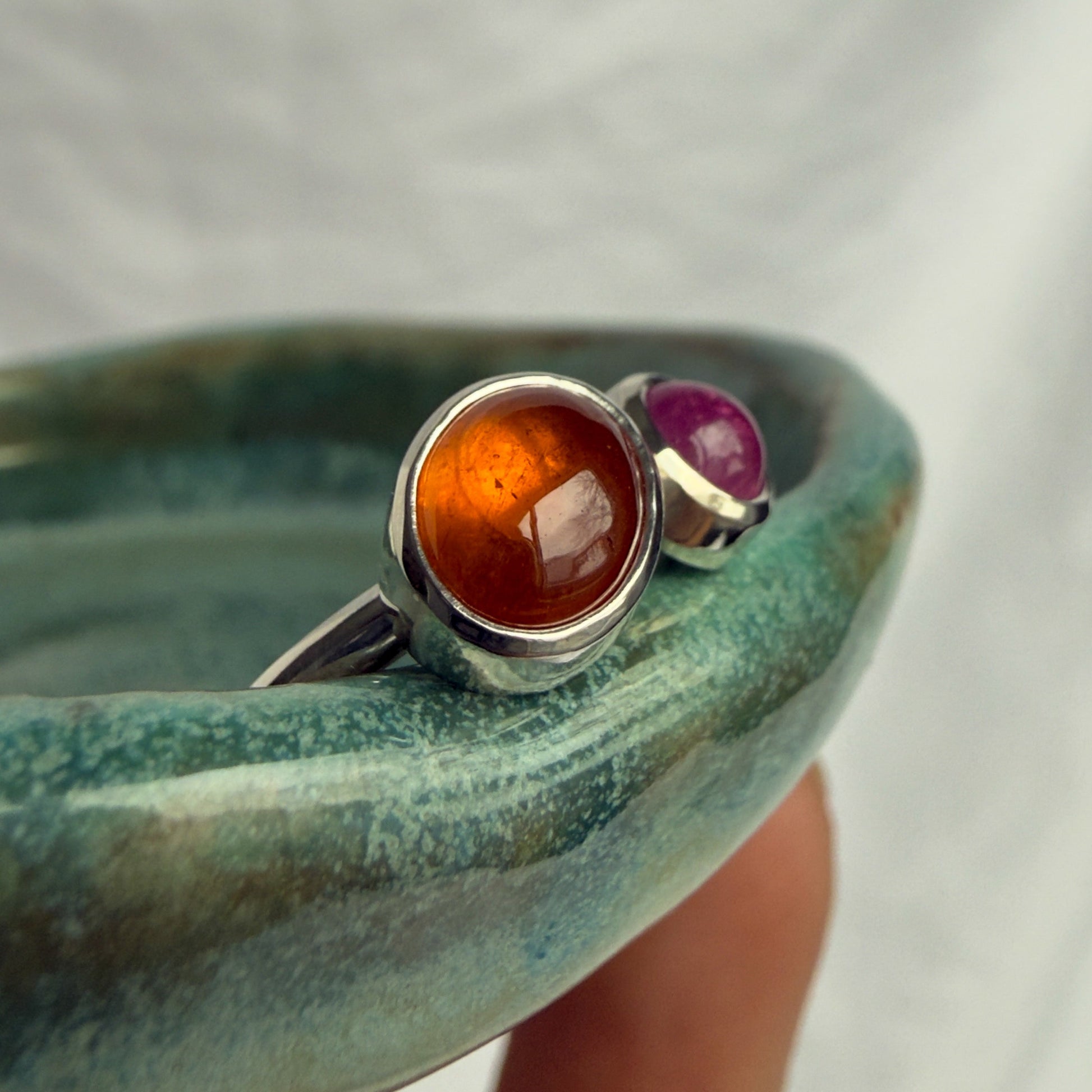 Silver ring with amber and ruby stones held on a textured surface
