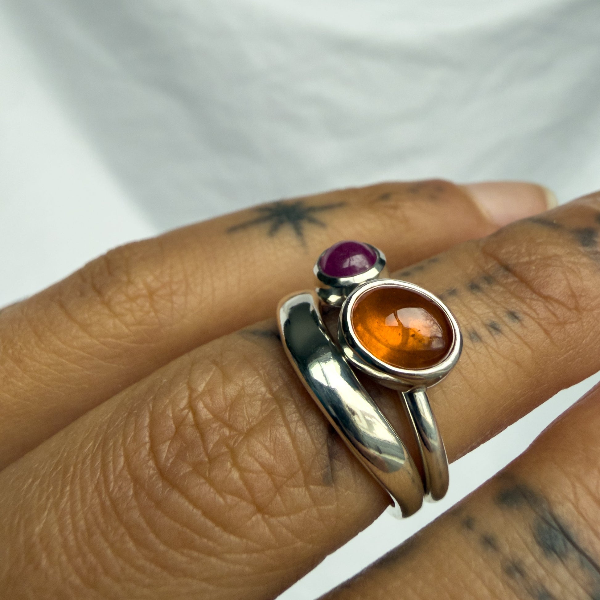 Silver ring with gemstones on a person's finger against a white background