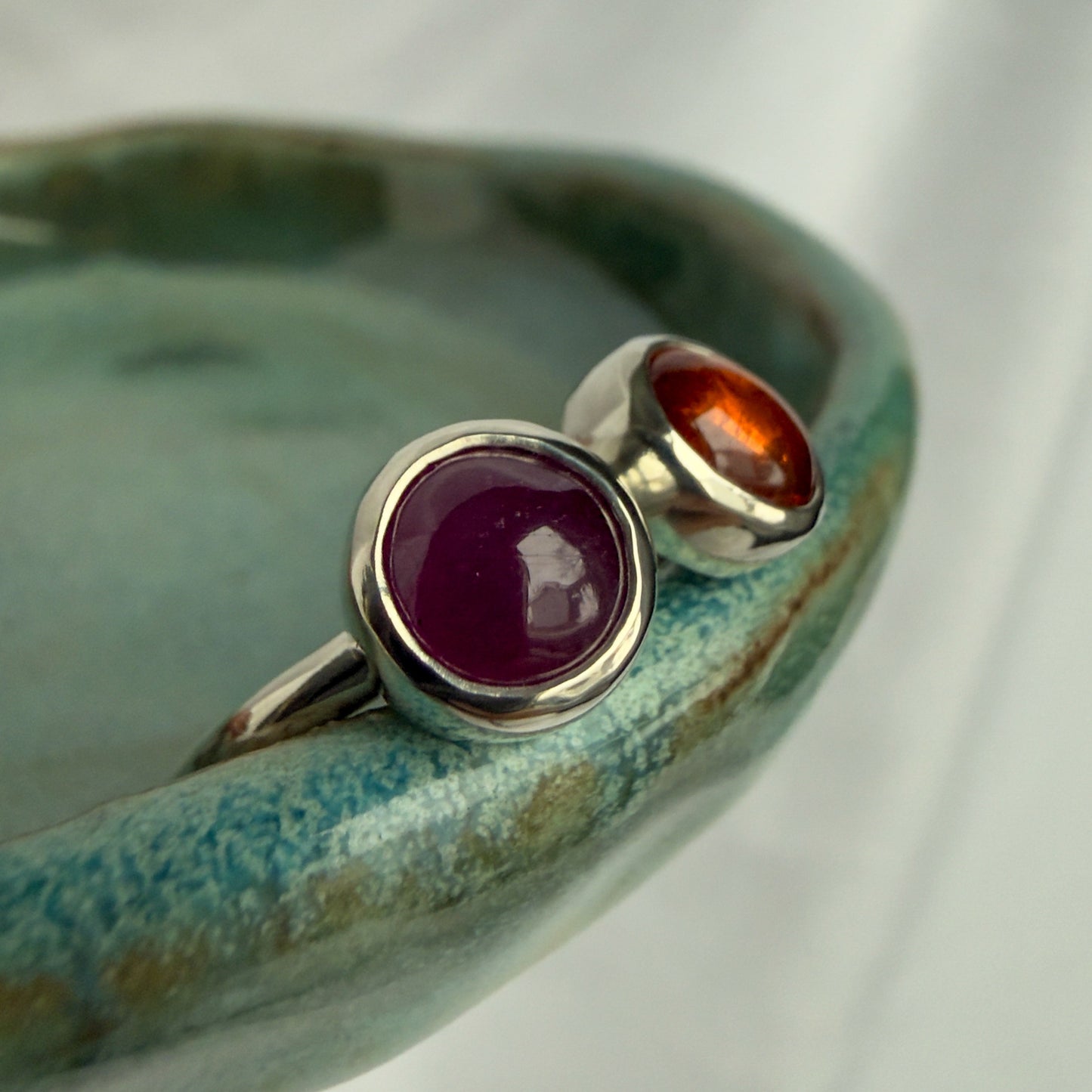 Two silver rings with gemstones on a ceramic dish