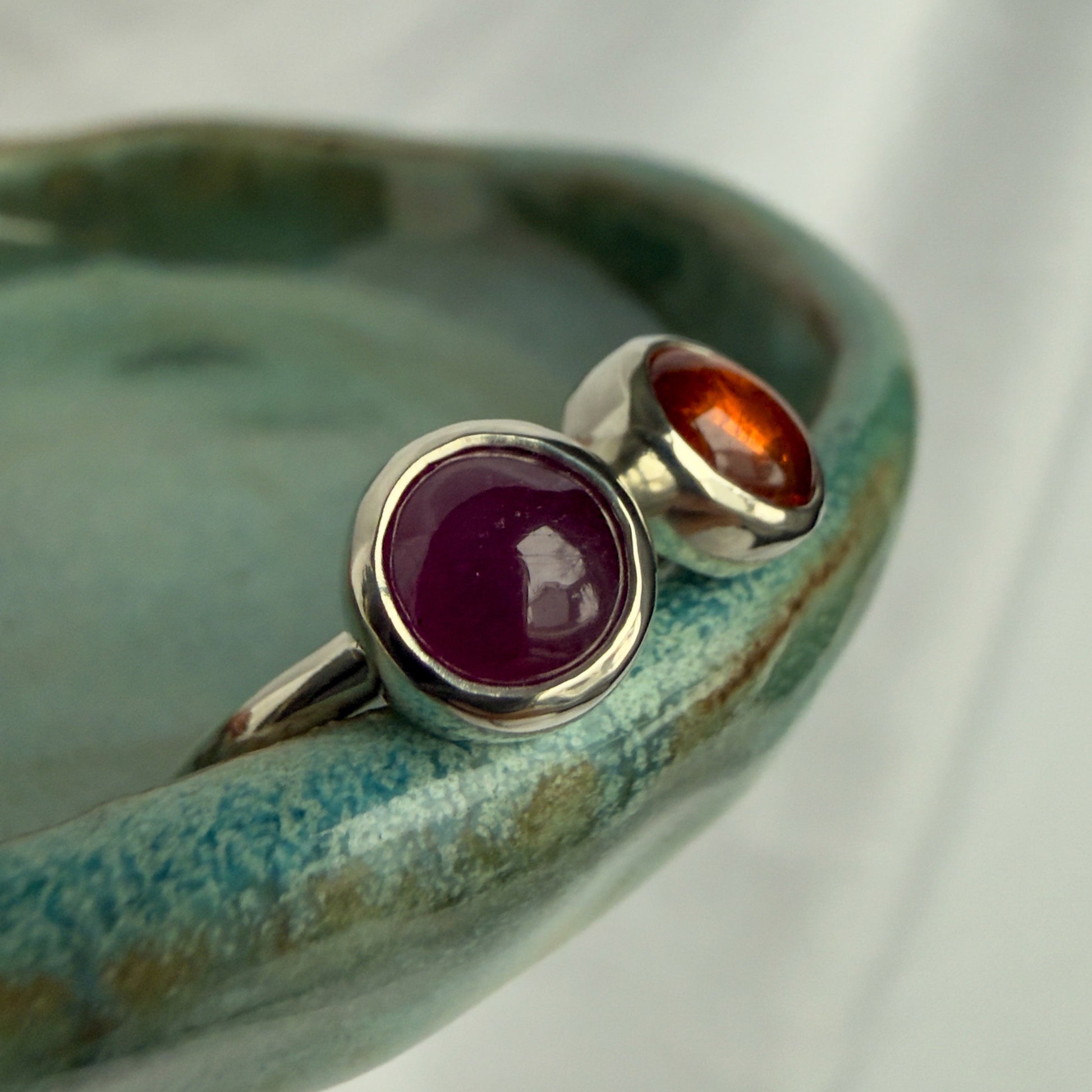 Two silver rings with gemstones on a ceramic dish