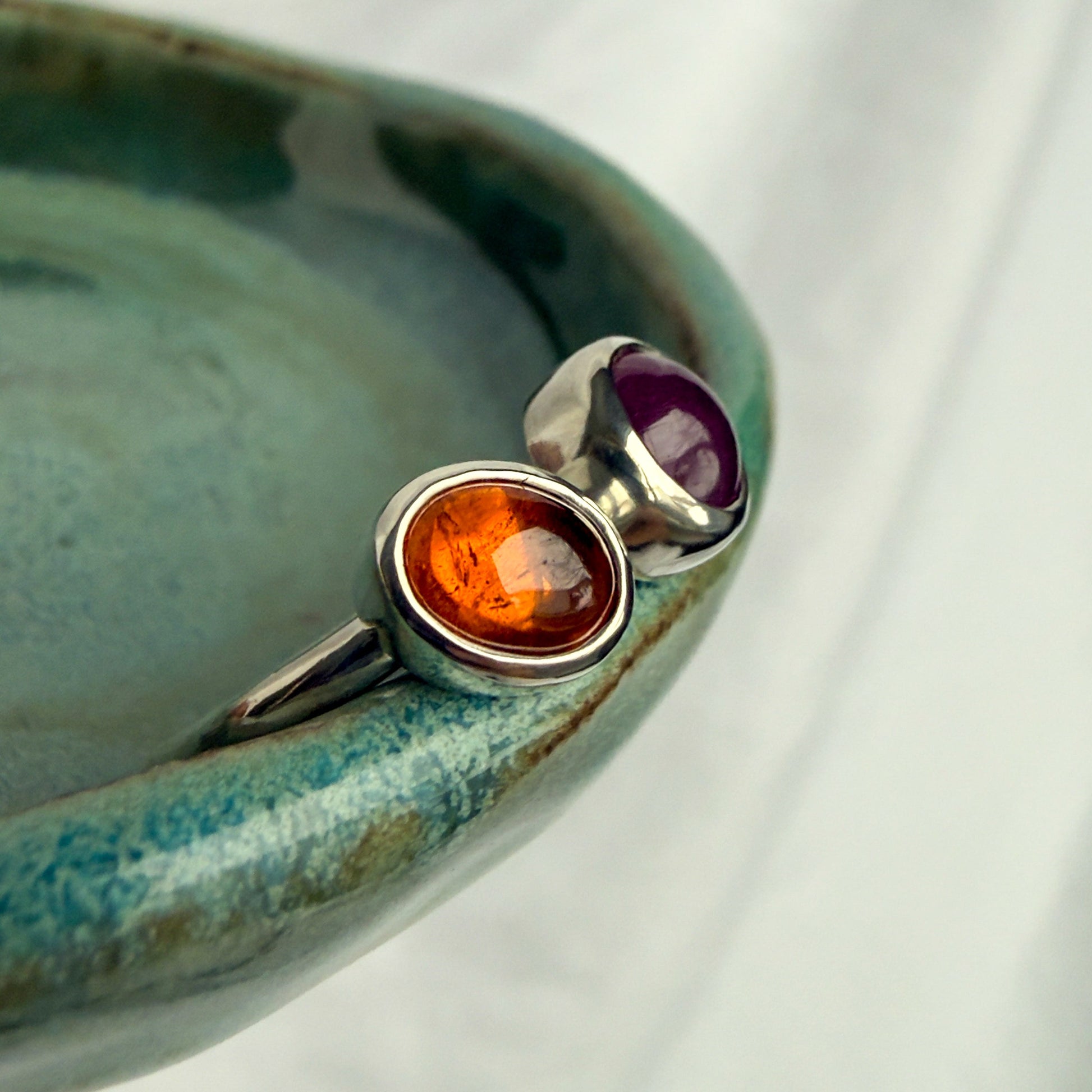 Silver ring with amber and amethyst stones on a ceramic dish