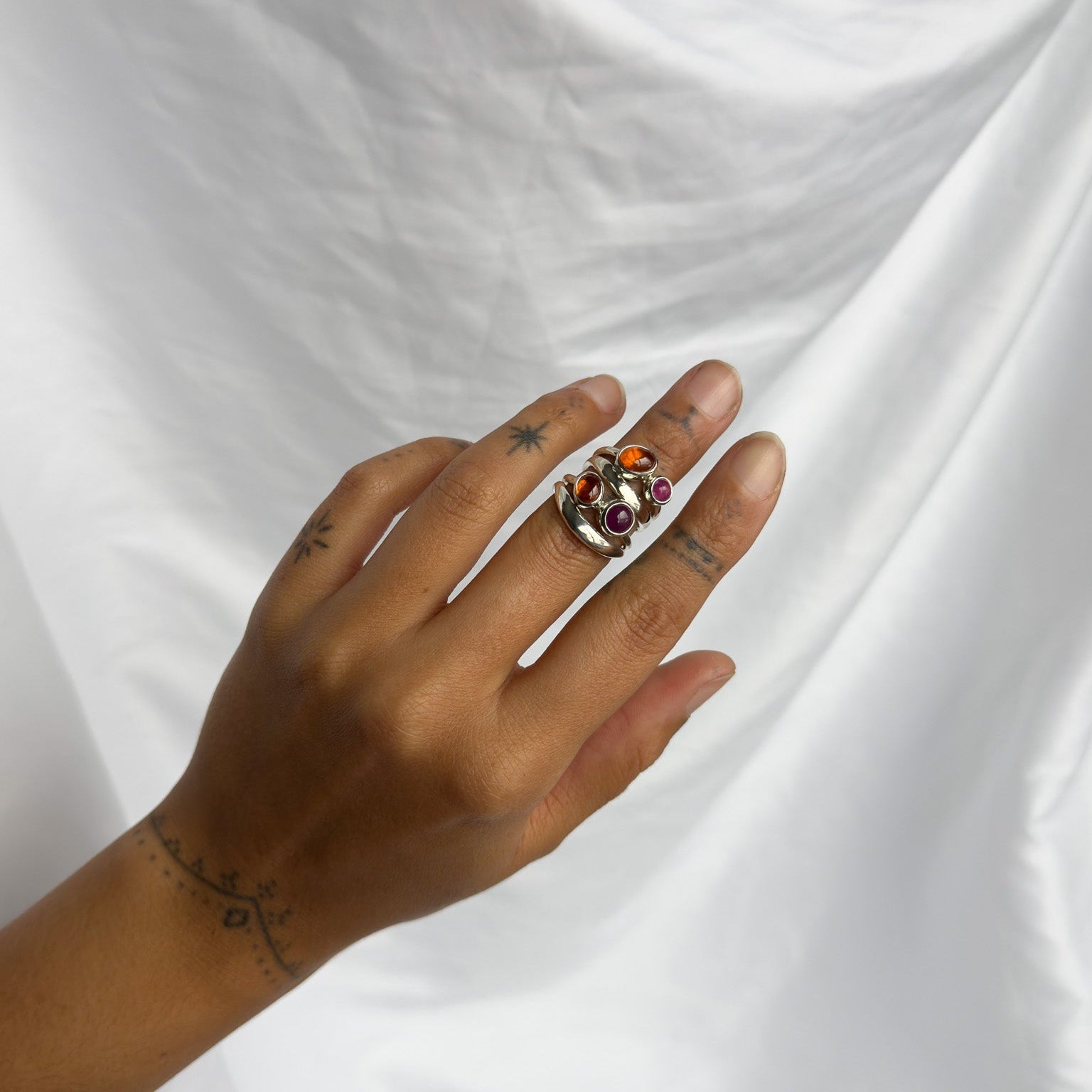 Hand wearing a ring with gemstones on a white fabric background