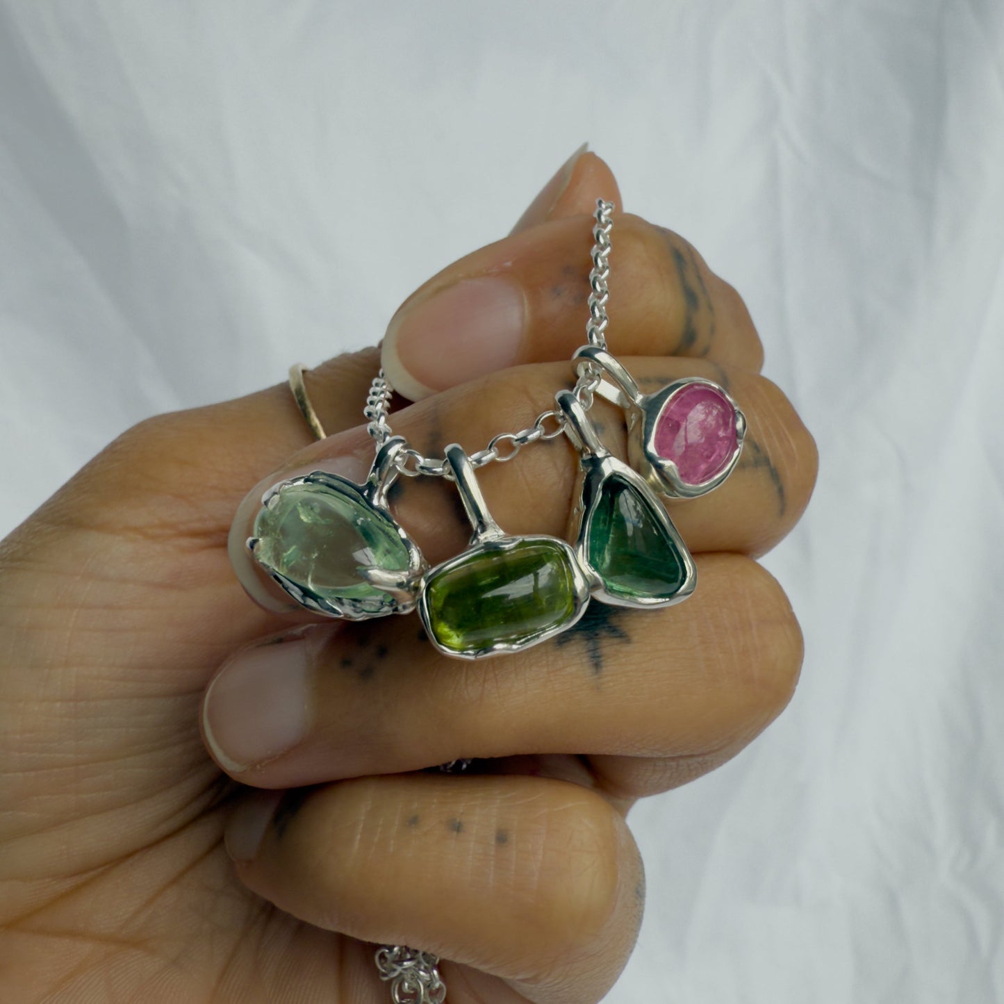 Hand holding a silver necklace with green and pink tourmaline gemstones against a white background