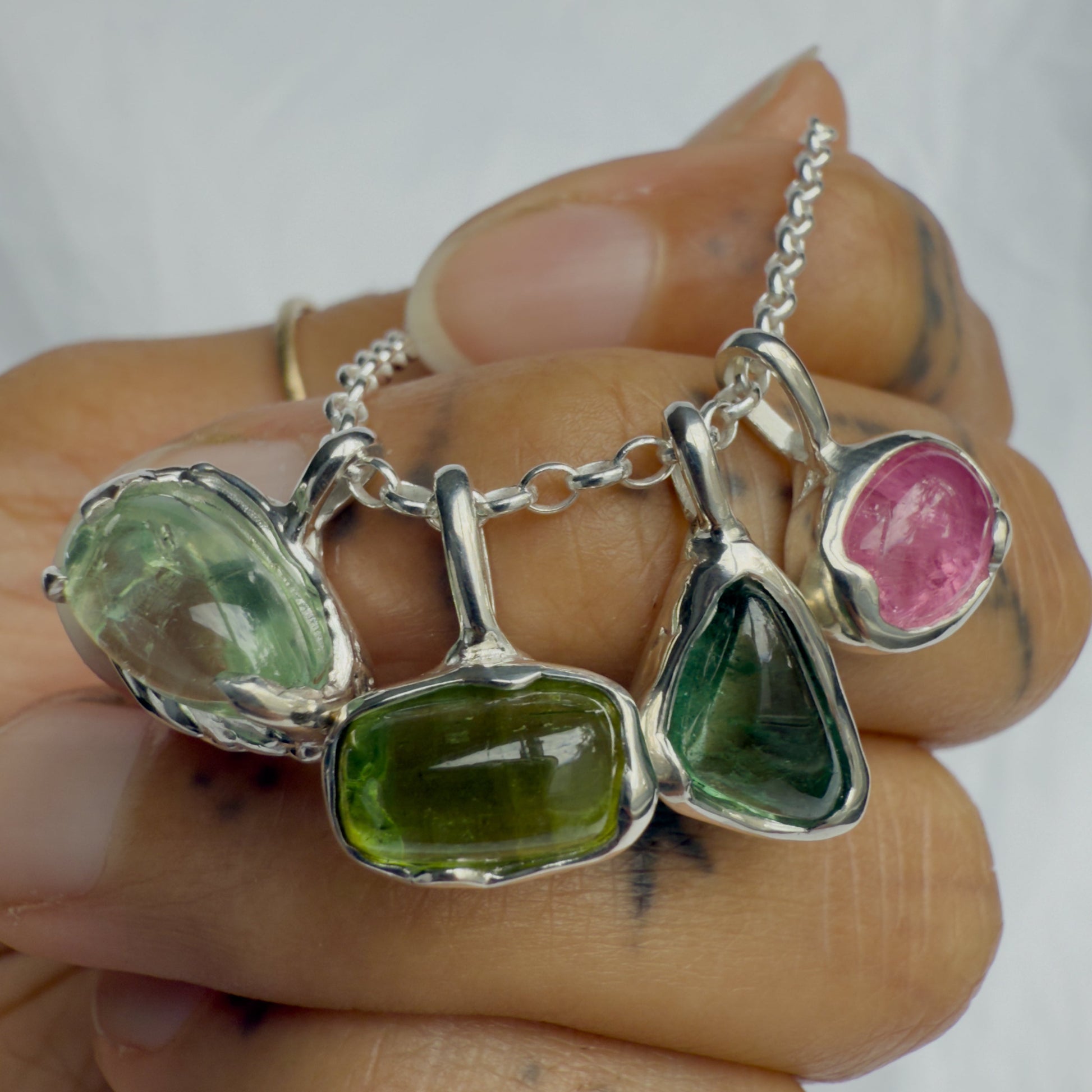Jewelry set with green and pink tourmaline gemstones on a hand against a white background