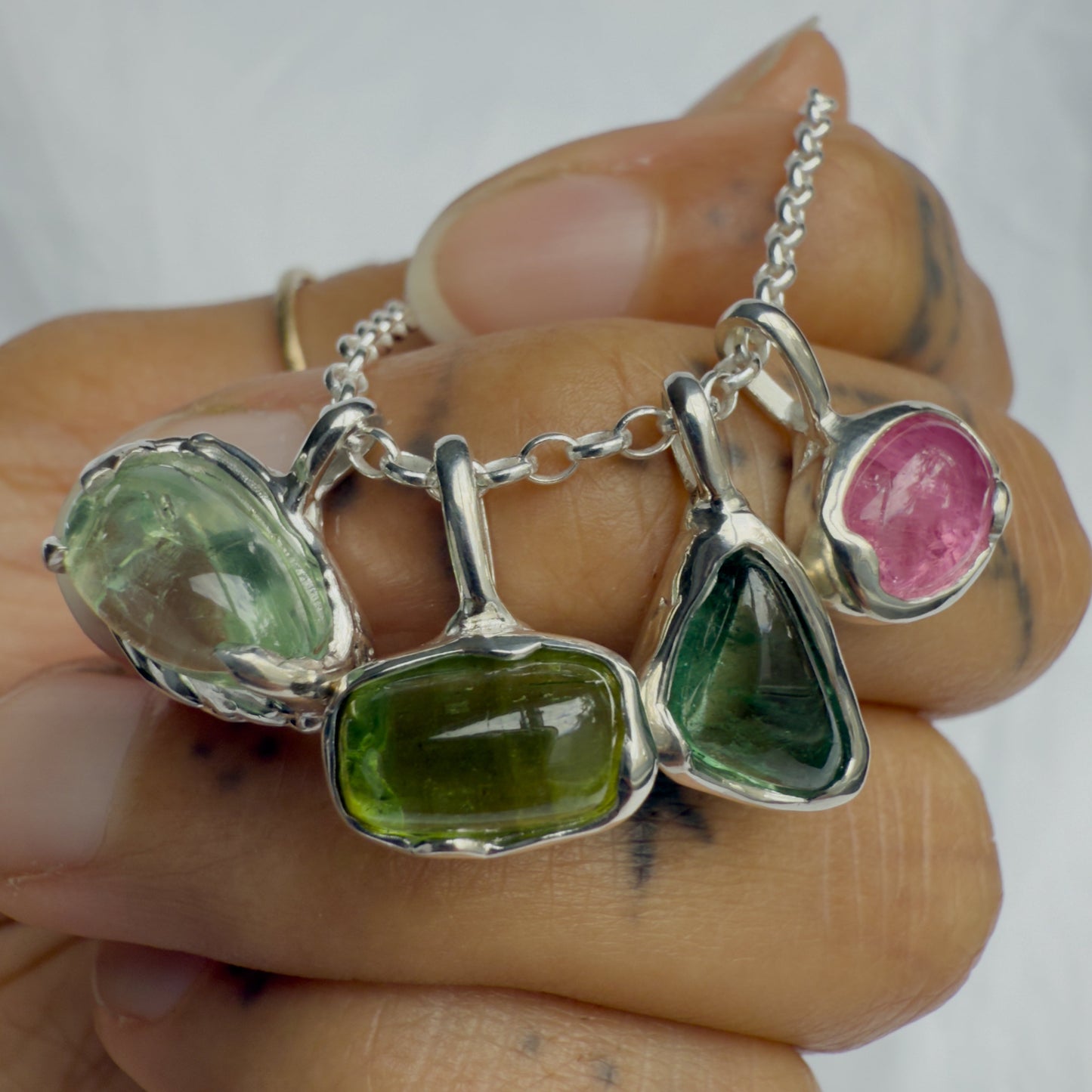 Jewelry set with green and pink tourmaline gemstones on a hand against a white background