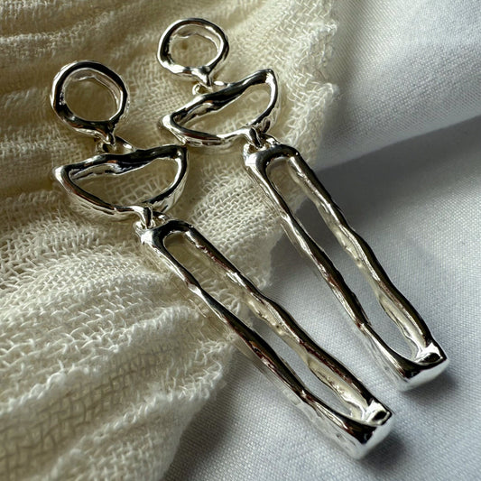 Silver abstract moon earrings on a textured fabric background