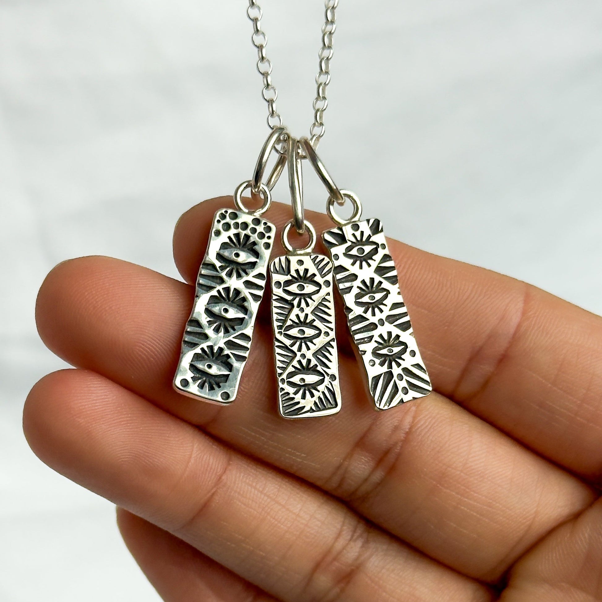 Silver necklace with three patterned pendants held in a hand against a white background
