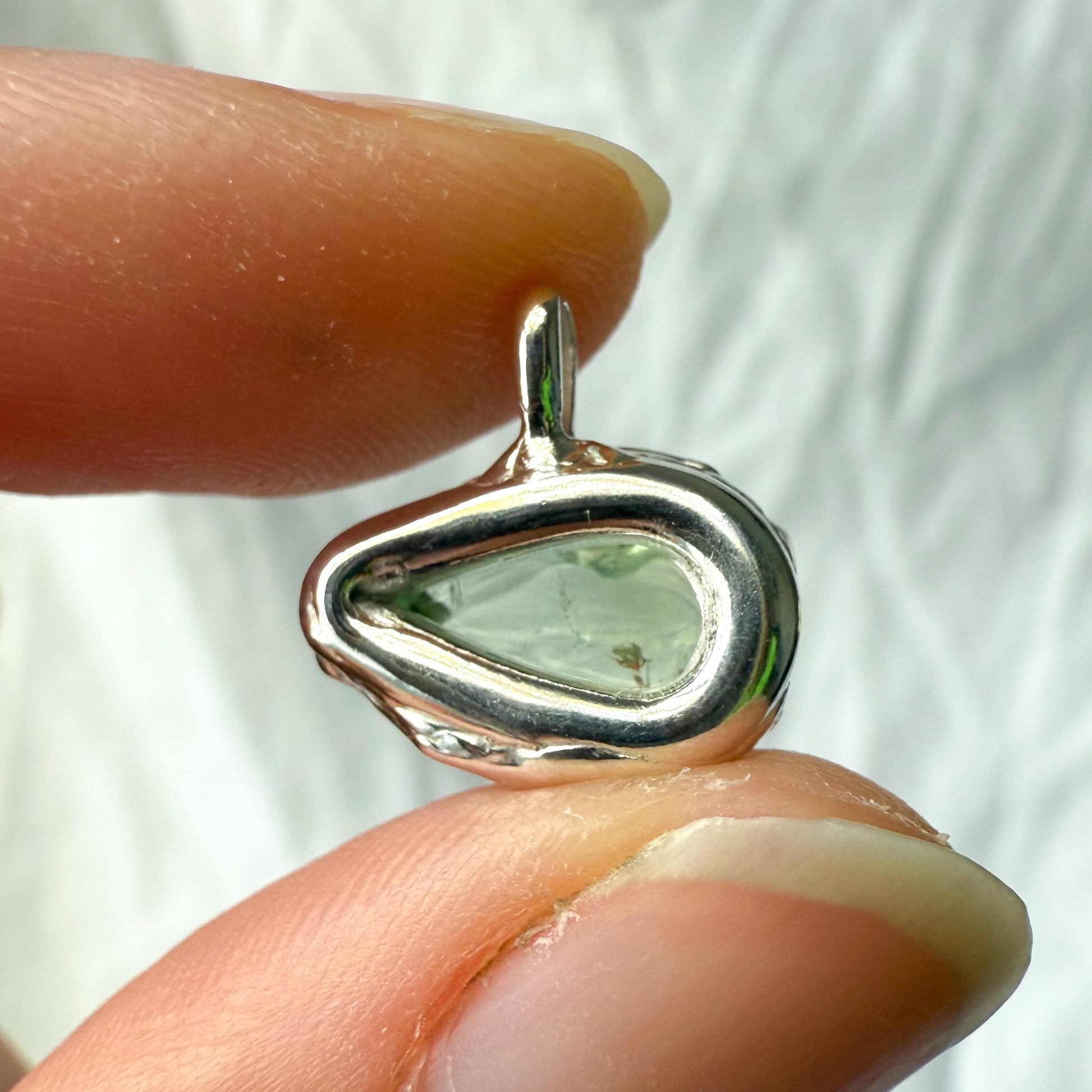 Silver pendant with a green tourmaline gemstone held between fingers against a white background