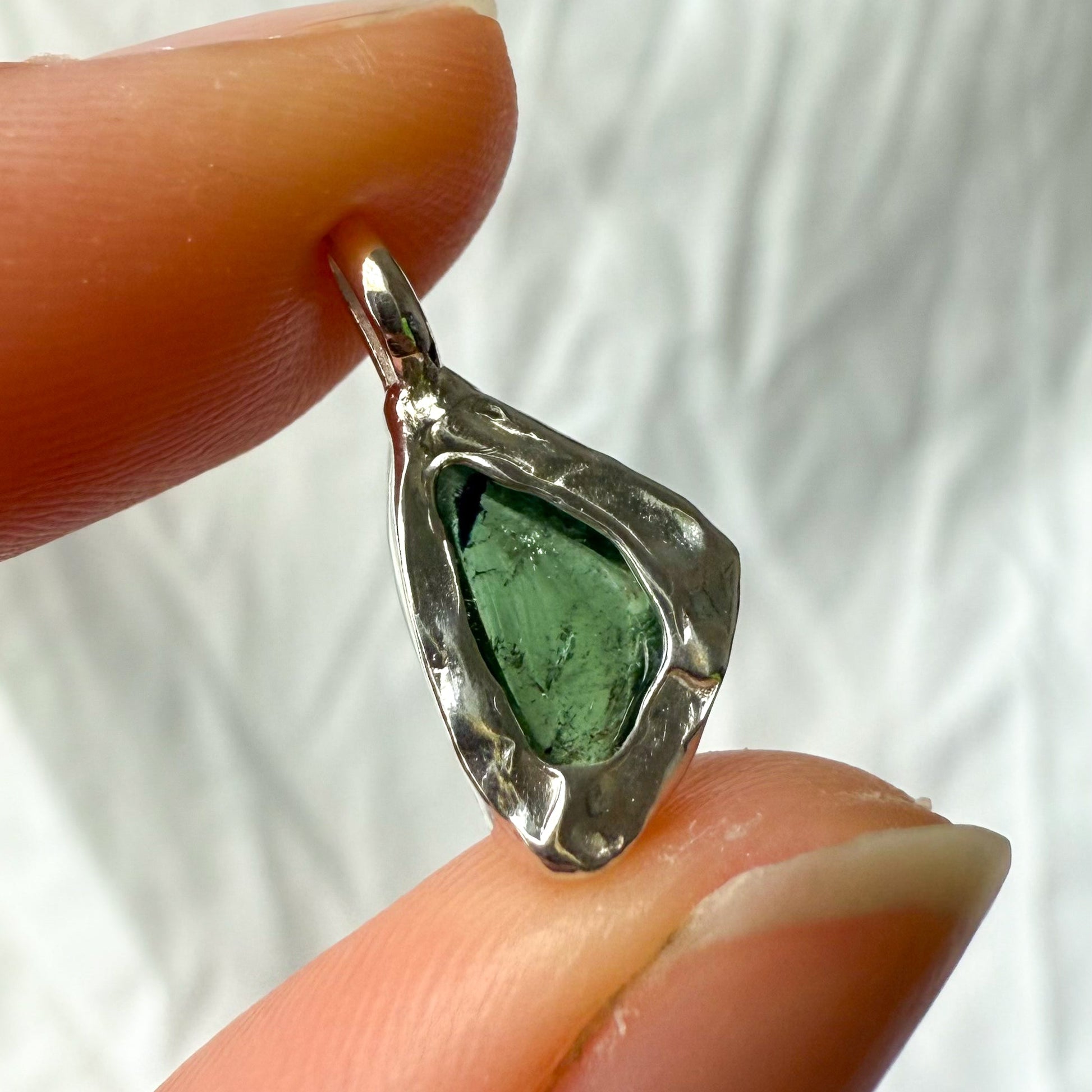 Silver pendant with green tourmaline held between fingers against a white background