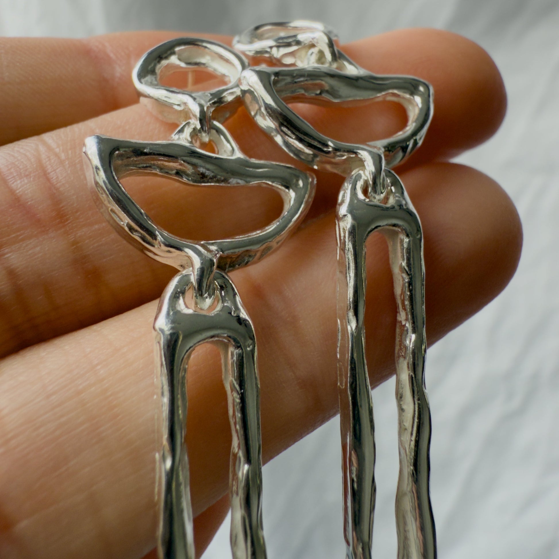 Silver moon earrings held between fingers against a neutral background