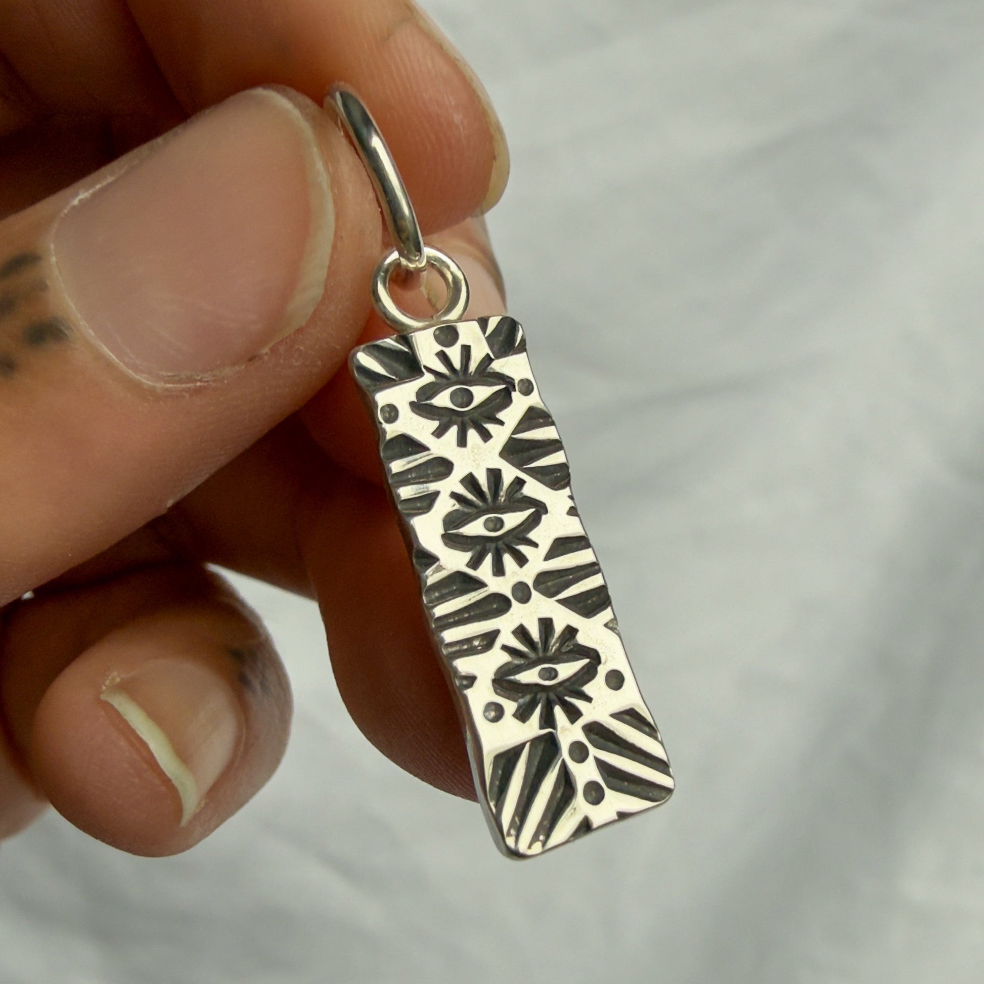 Silver pendant with intricate patterns held by a hand against a plain background