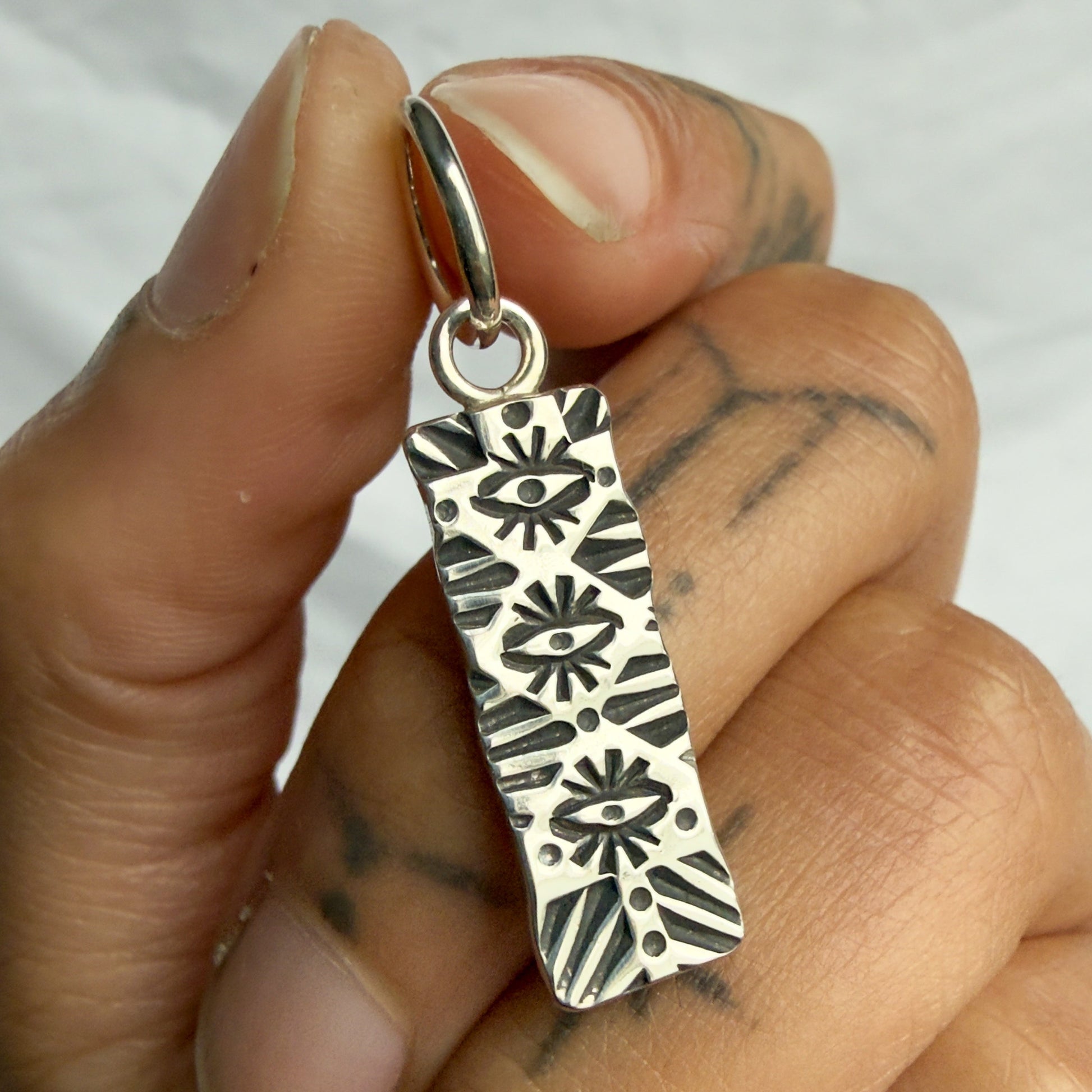 Hand holding a silver pendant with intricate designs against a neutral background