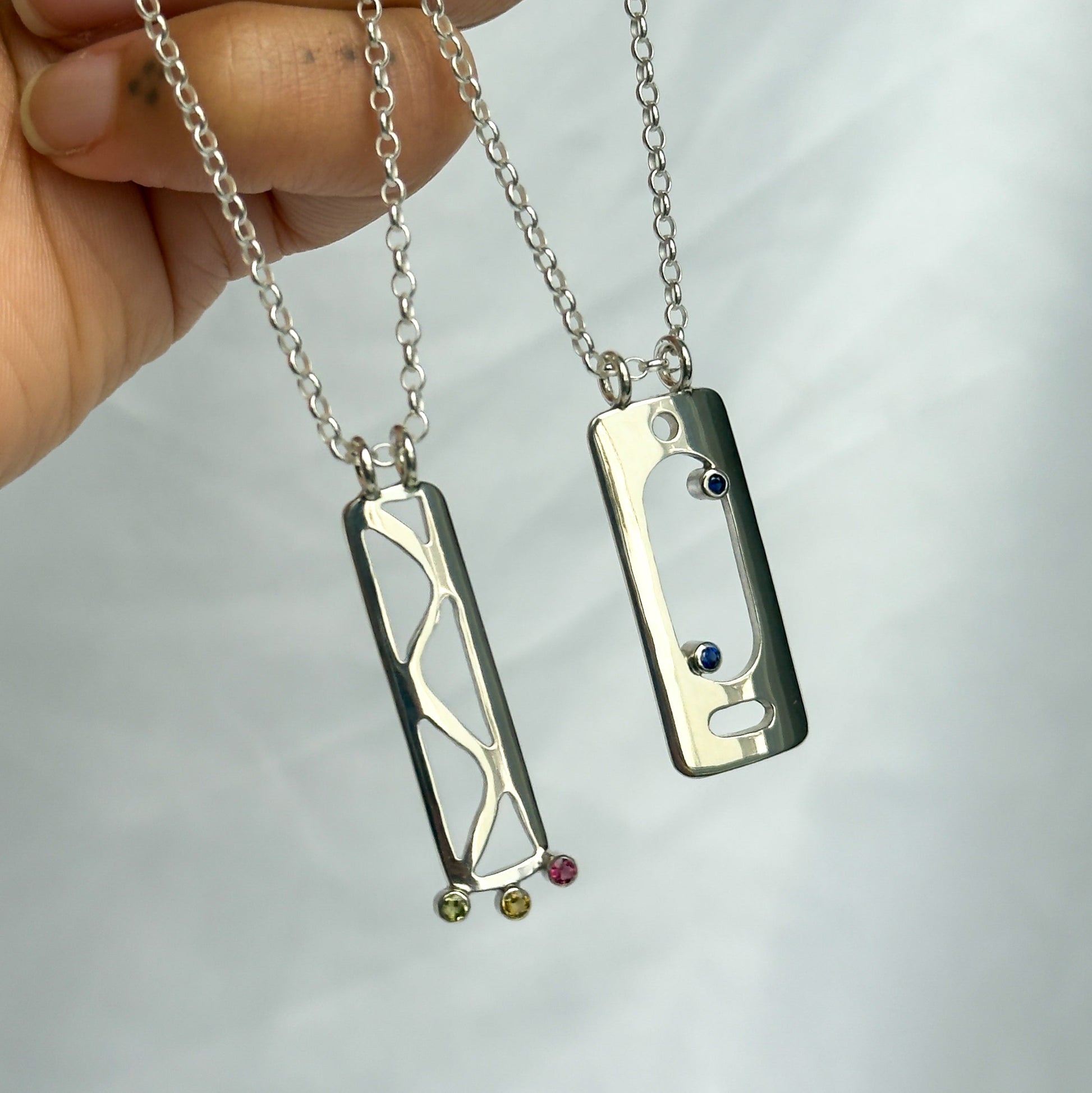 Two silver necklaces with pendants held by a hand against a white background