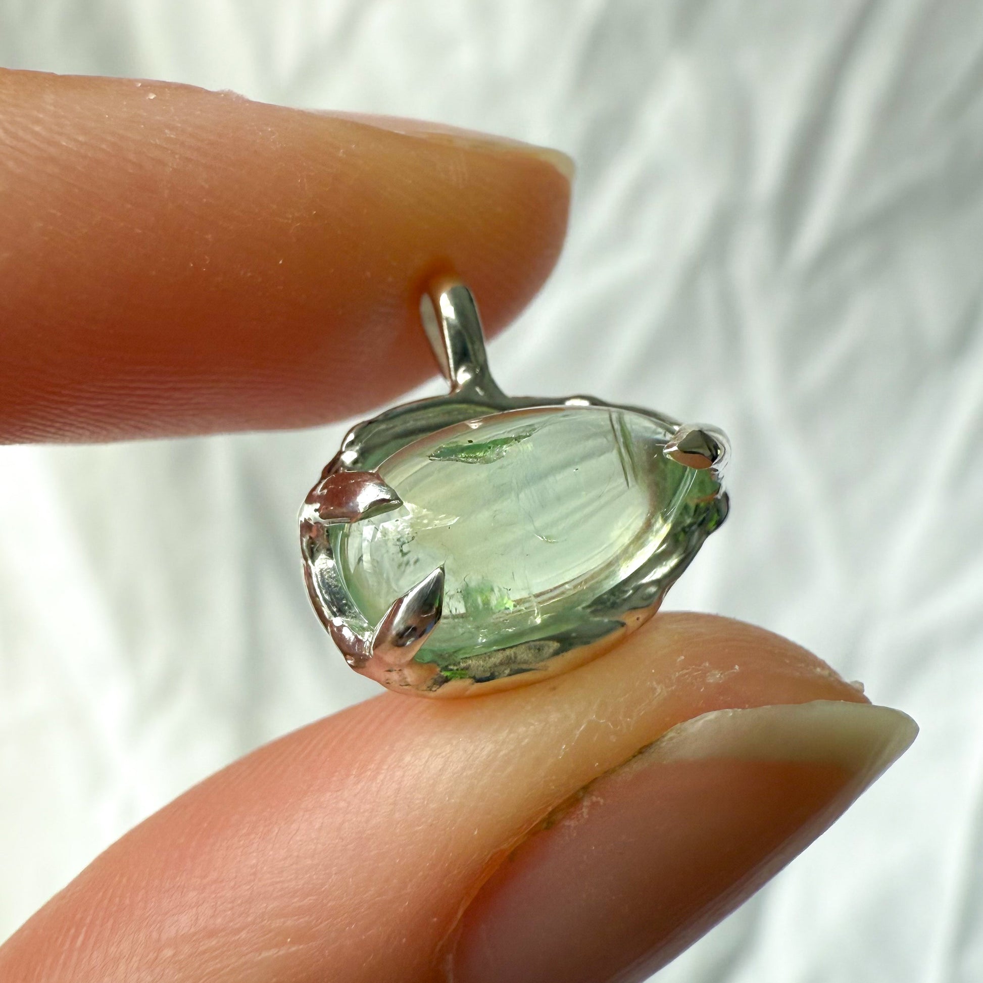 Green tourmaline gemstone pendant held between fingers against a white background