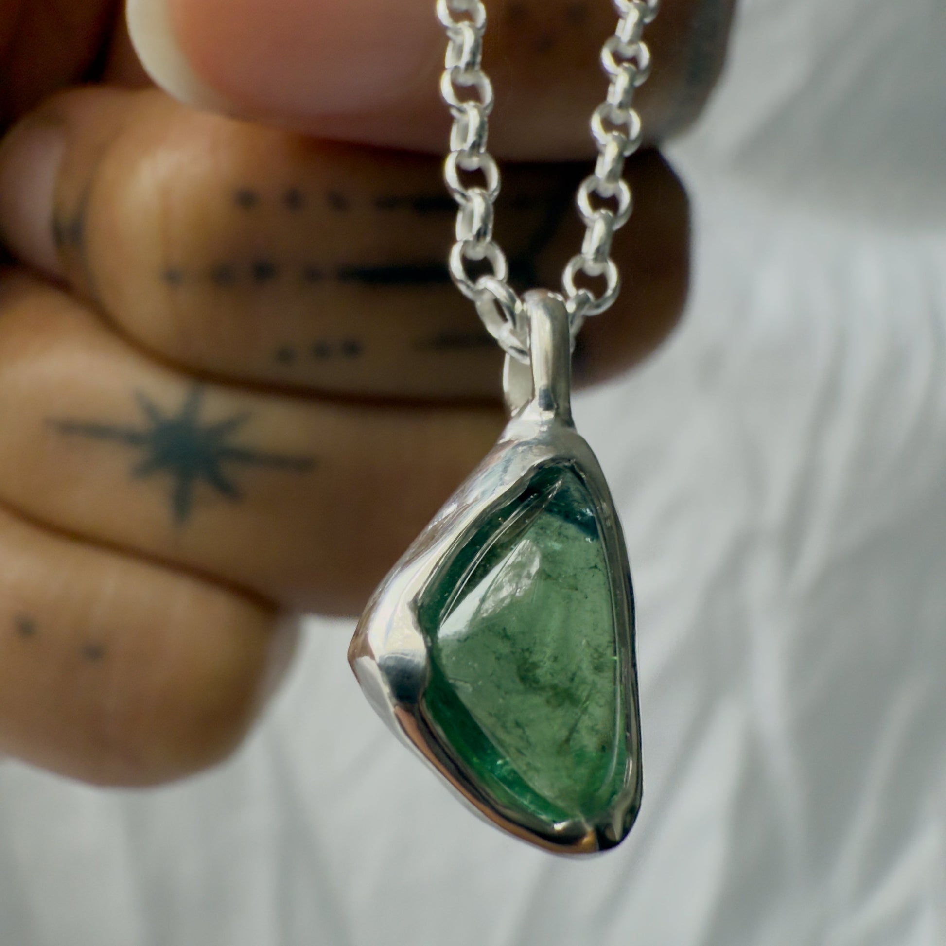 Green teardrop tourmaline pendant on a silver chain held by a hand with a tattoo.