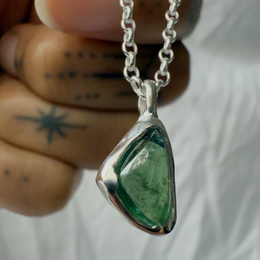Green teardrop tourmaline pendant on a silver chain held by a hand with a tattoo.