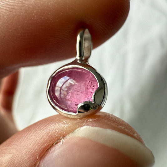 Pink tourmaline gemstone pendant held between fingers against a neutral background