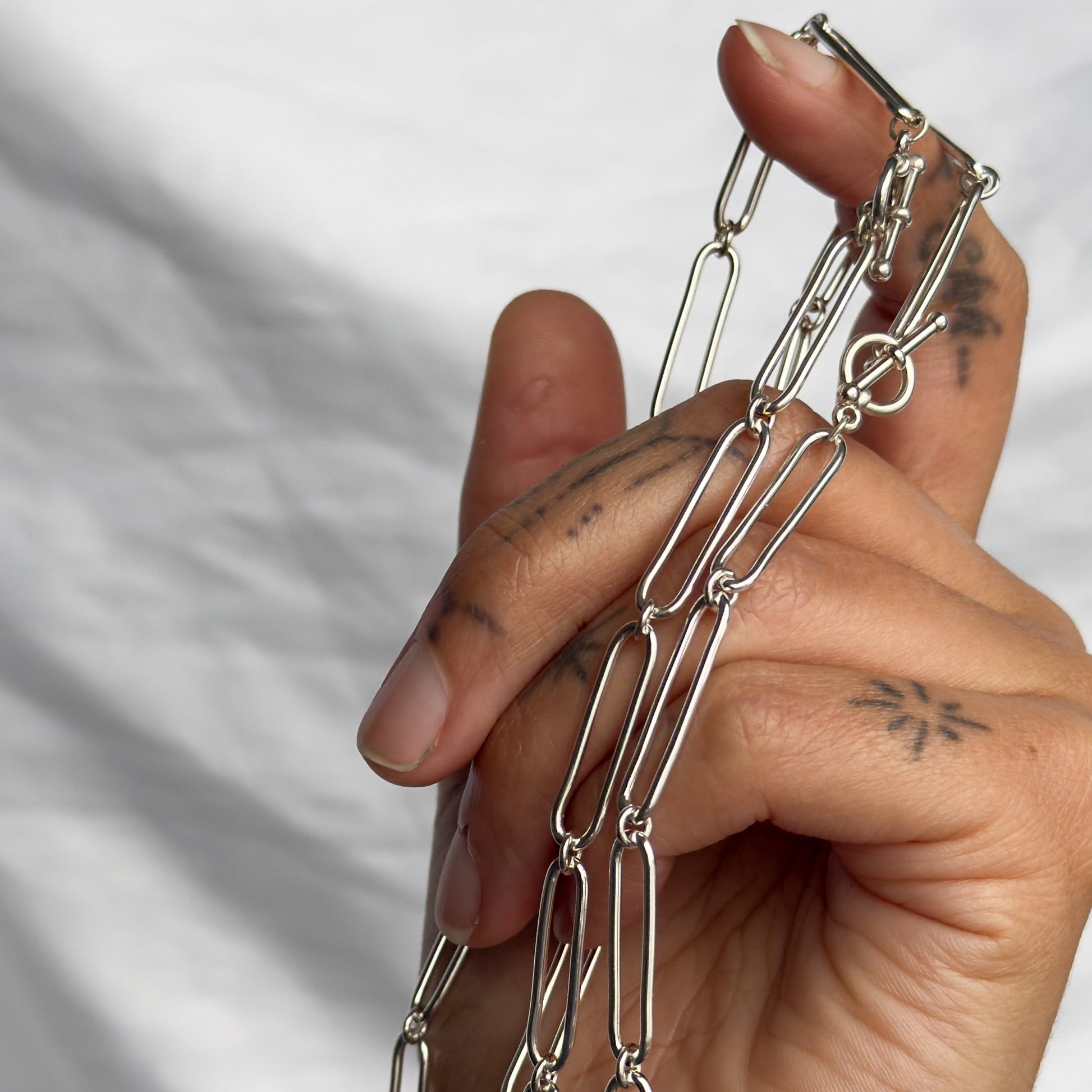 Hand holding a silver chain necklace against a neutral background