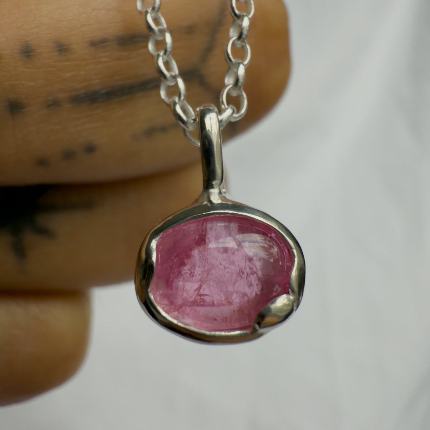 Pink tourmaline stone pendant on a silver chain held by a hand against a white background