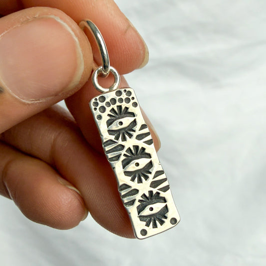 Silver pendant with eye design held by a hand against a white background