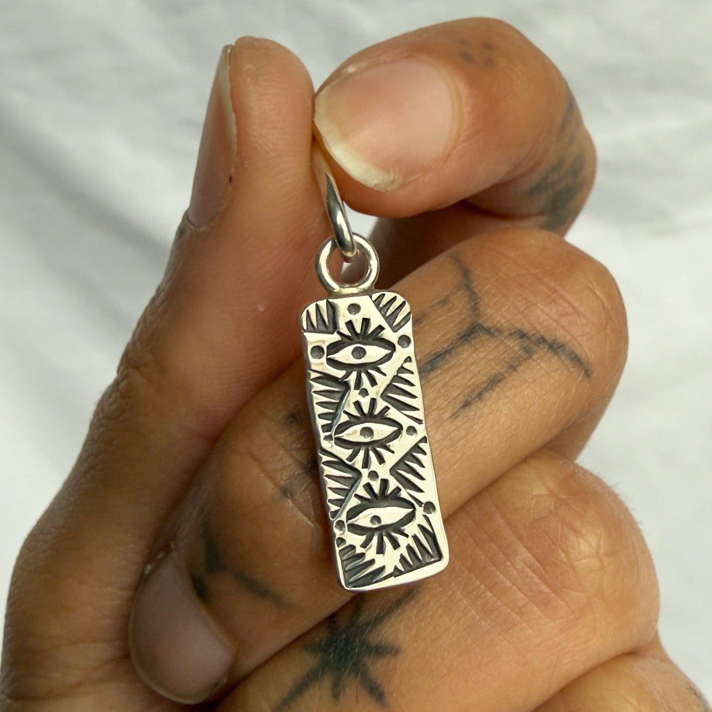 Hand holding a silver pendant with intricate designs against a neutral background