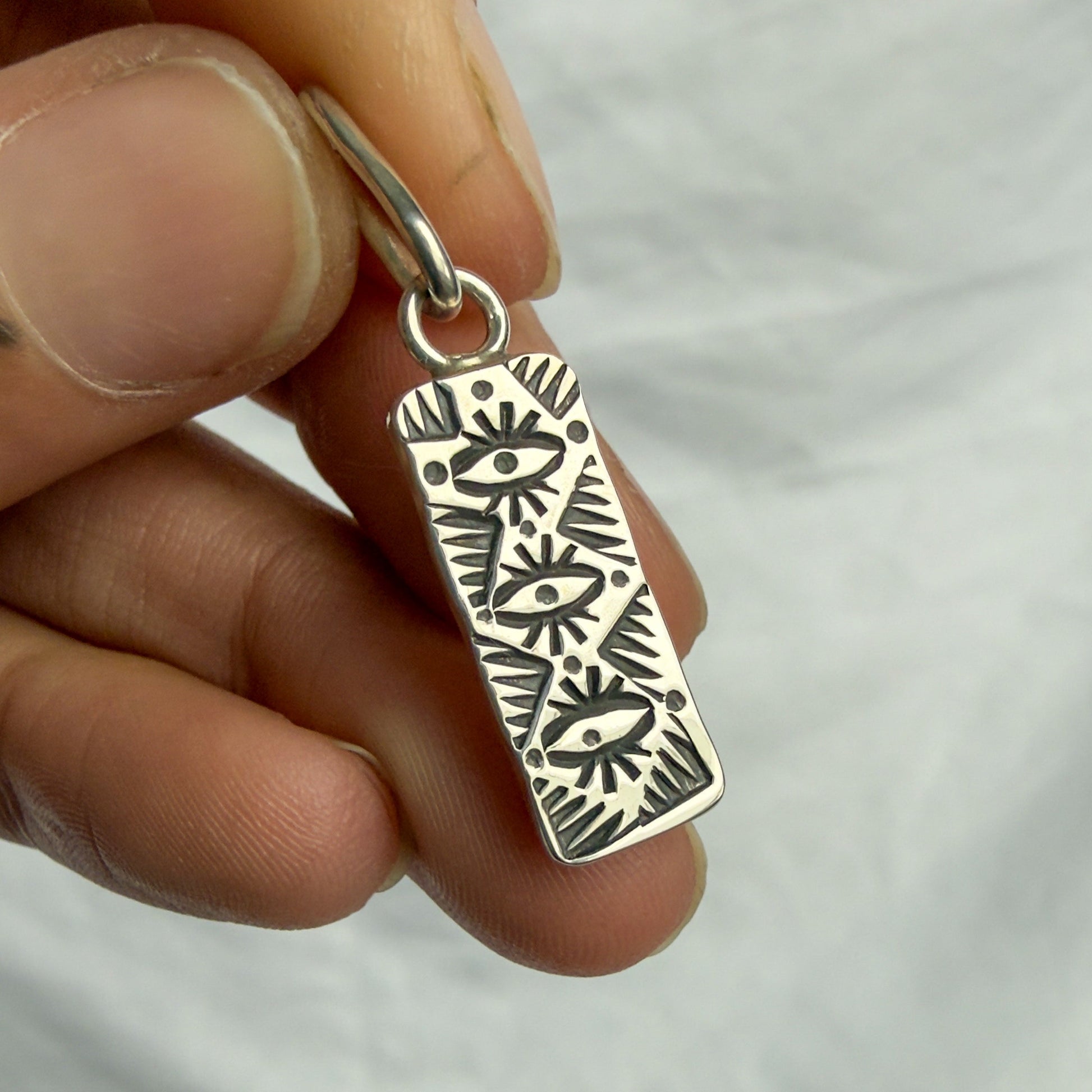Silver pendant with intricate patterns held by a hand against a white background