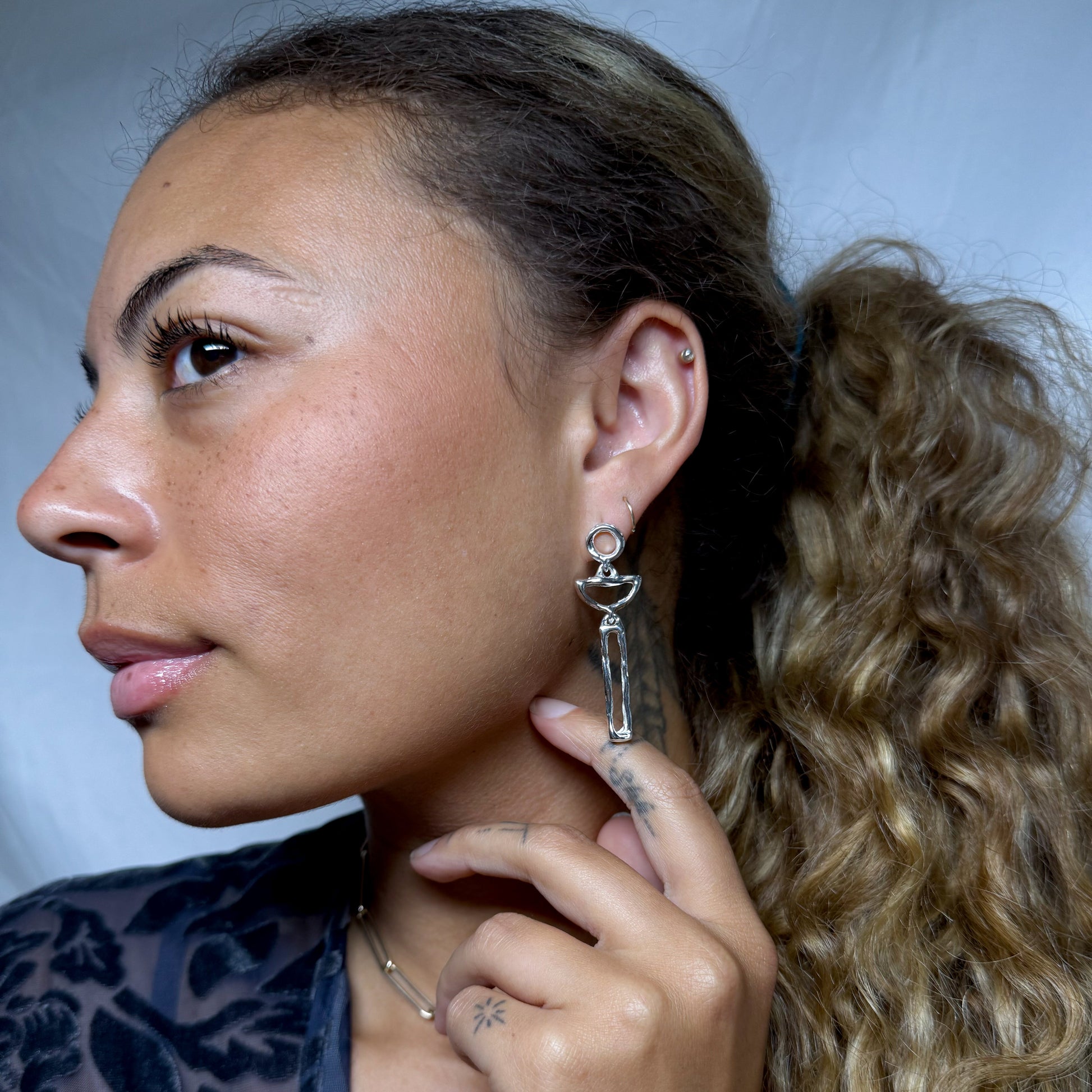 Woman wearing a unique earring with a small object attached, against a neutral background.