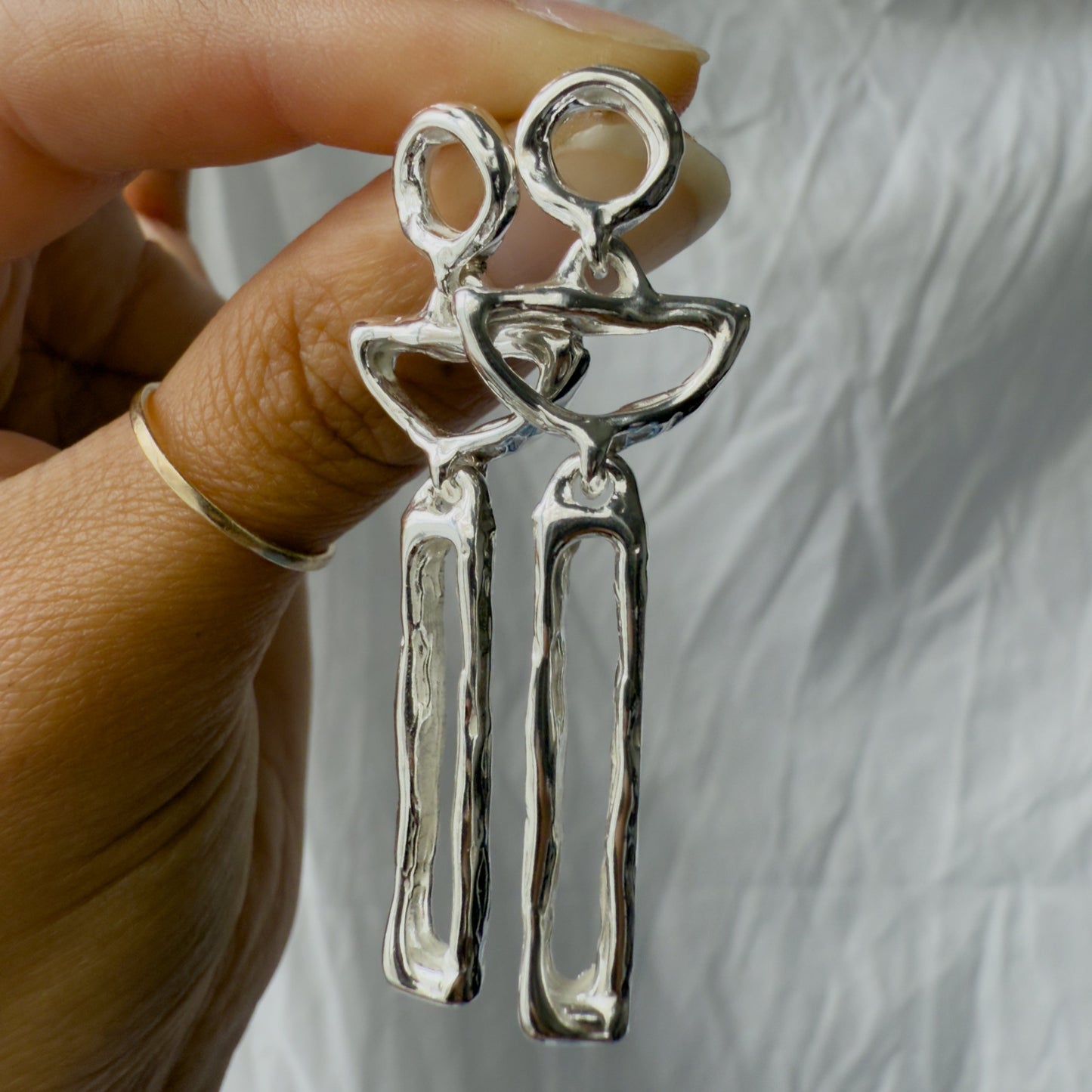 Silver moon earrings held by a hand against a neutral background