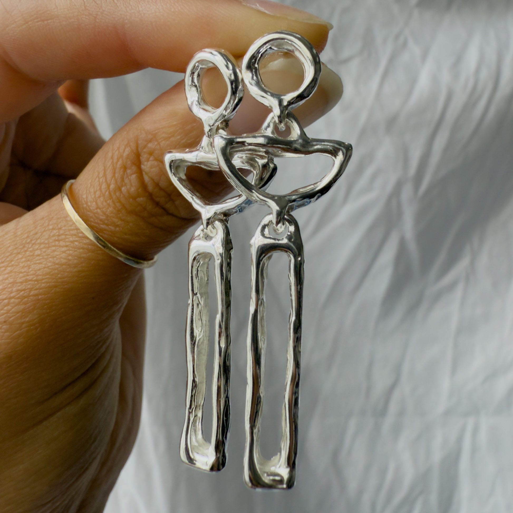 Silver moon earrings held by a hand against a neutral background