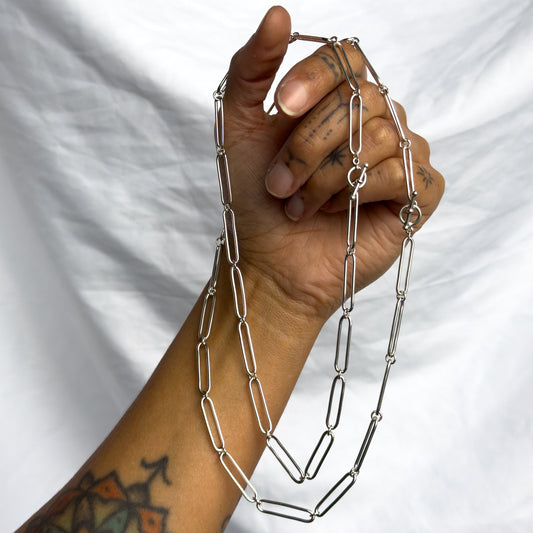 Hand holding a silver chain necklace against a white background