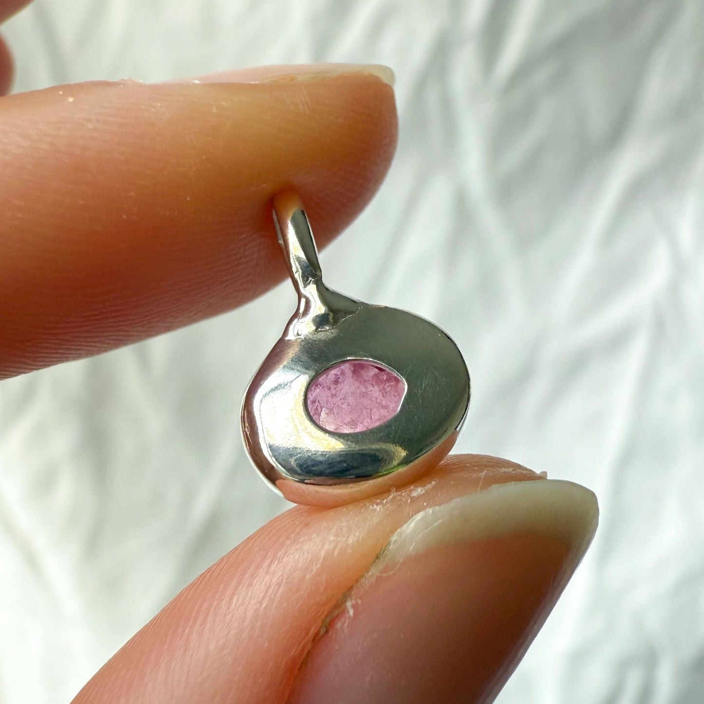 Silver pendant with a pink tourmaline stone held between two fingers against a white background