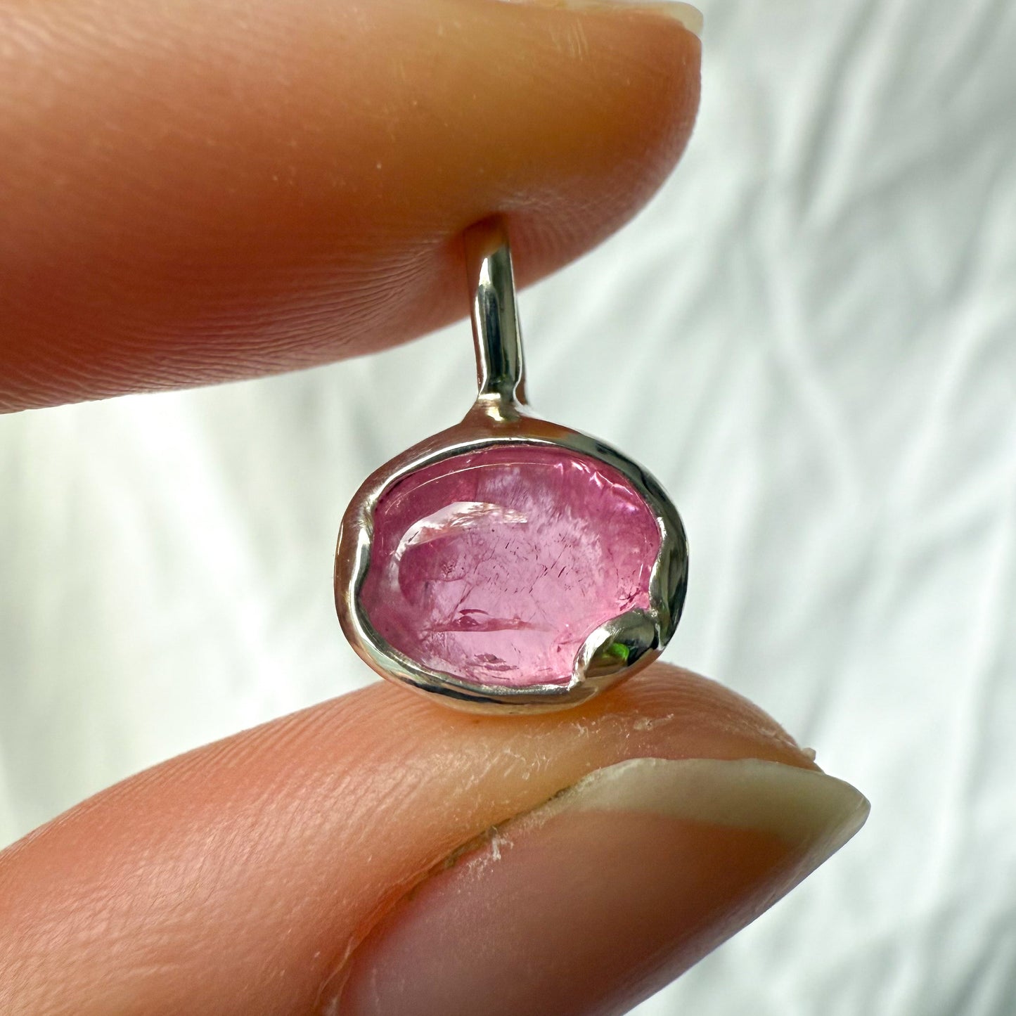 Pink tourmaline gemstone pendant held between fingers against a white background