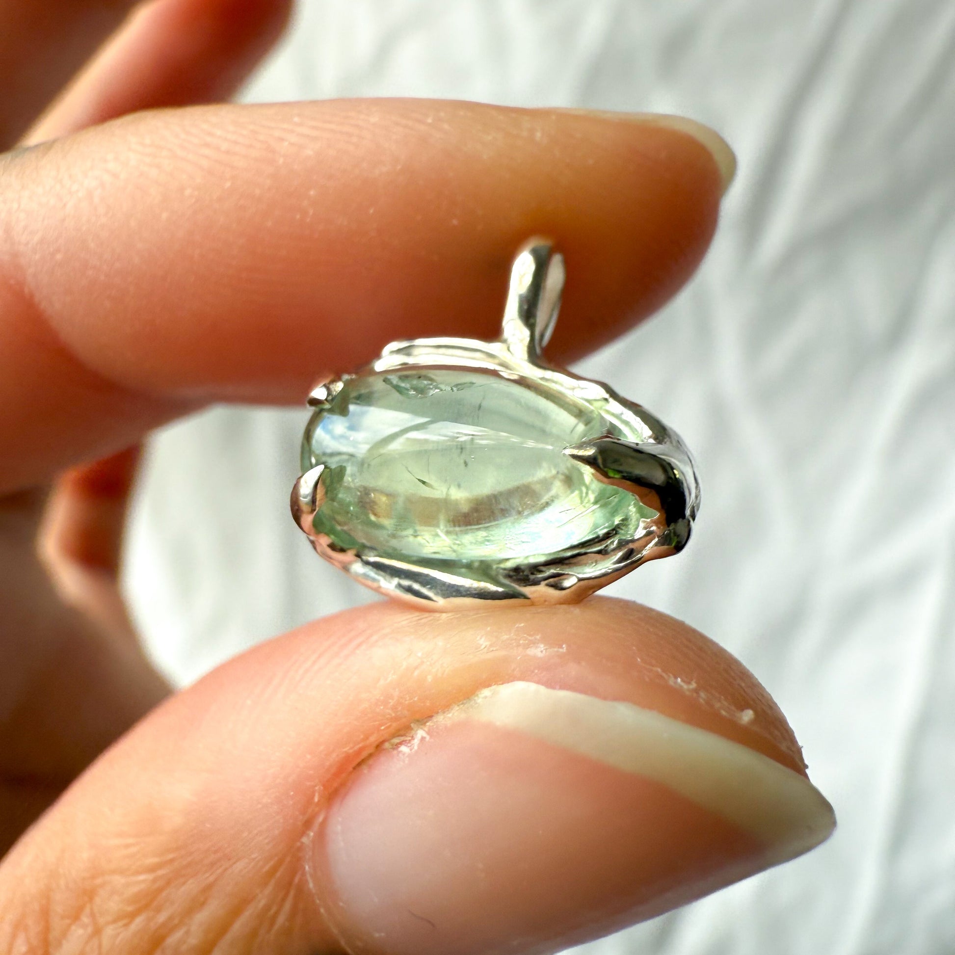 Green  tourmaline gemstone pendant held between fingers against a white background