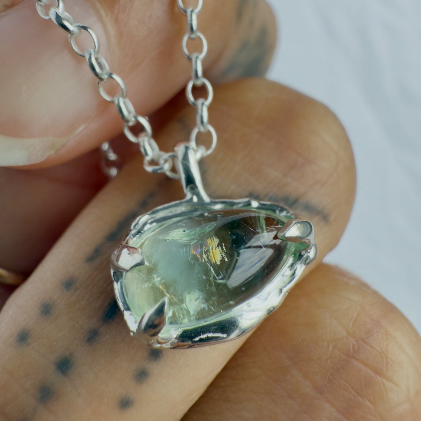 Silver pendant with a green tourmaline gemstone held between fingers