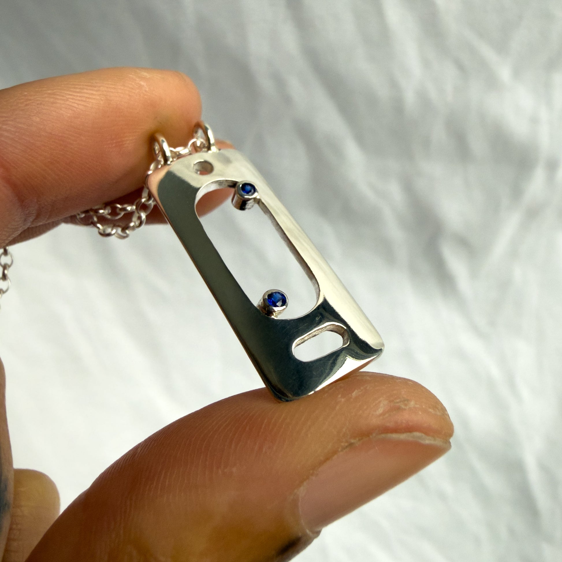 Hand holding a silver pendant with blue sapphire stones against a white background