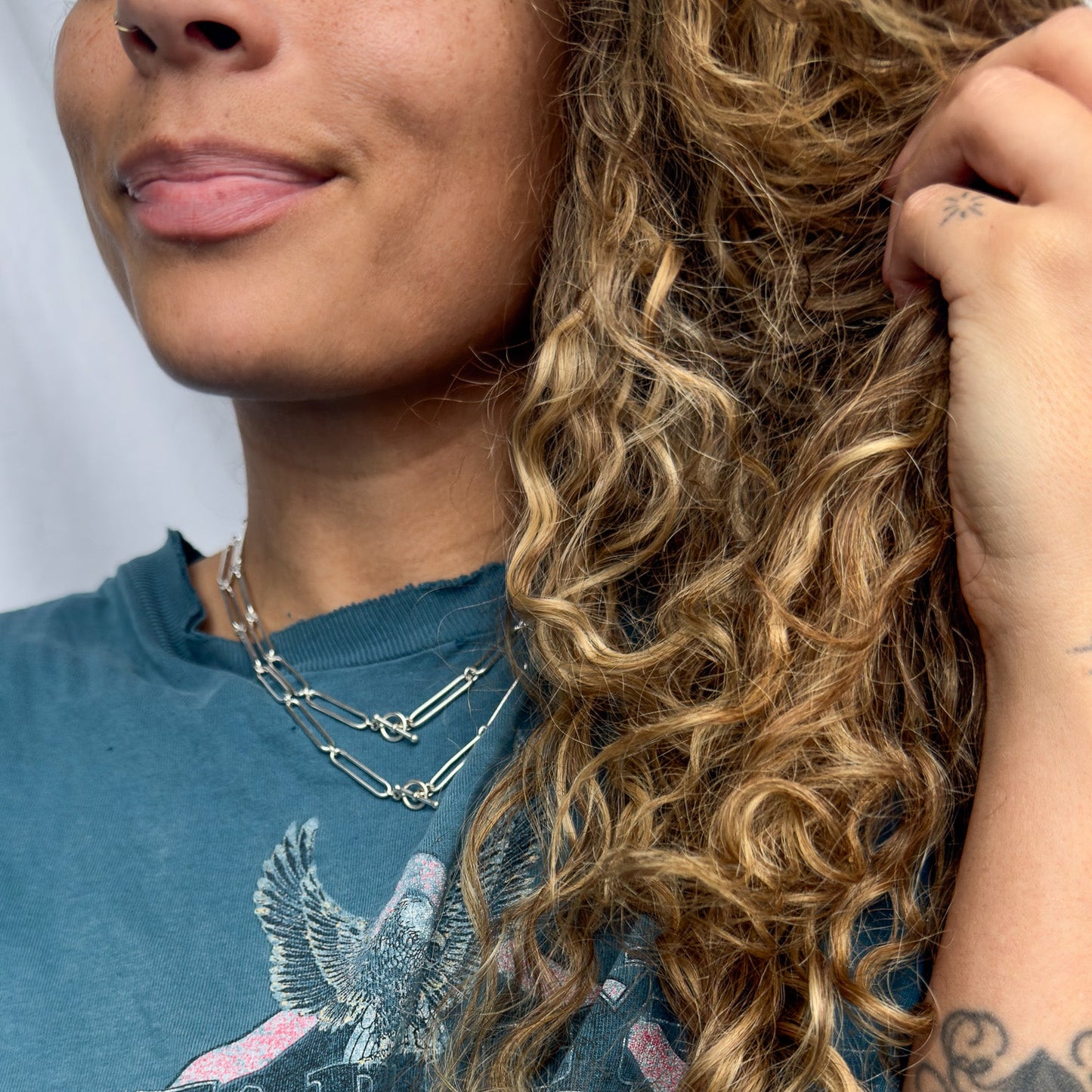 Woman wearing a blue t-shirt with a graphic design, smiling and touching her hair.