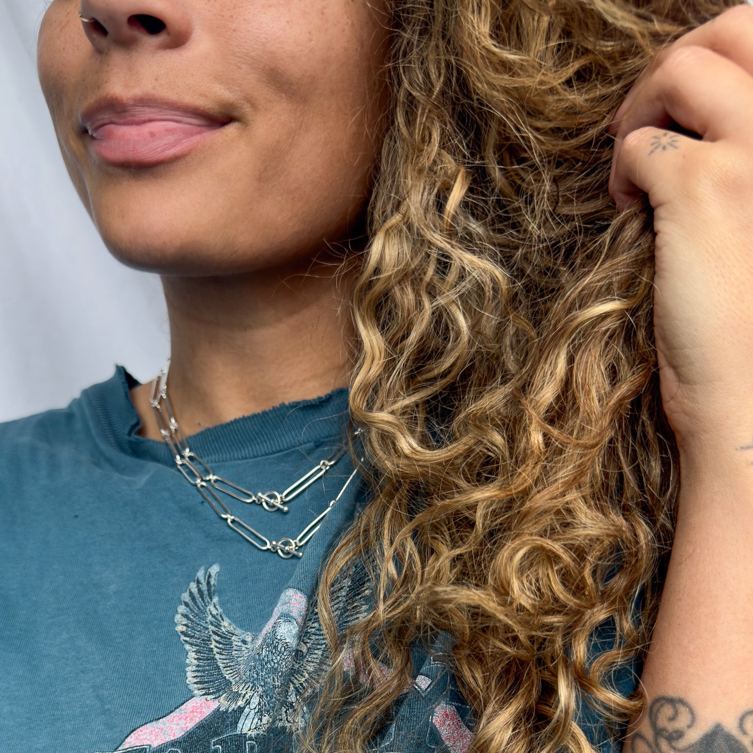Woman wearing a blue t-shirt with a graphic design, smiling and touching her hair.